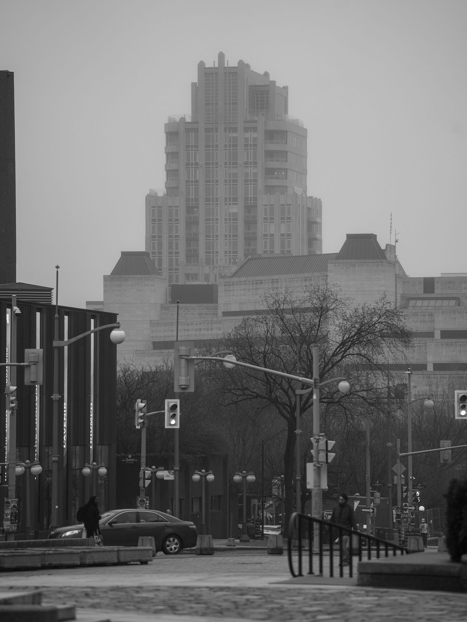 Foggy black and white cityscape with a tall Art Deco skyscraper looming over an empty urban plaza.