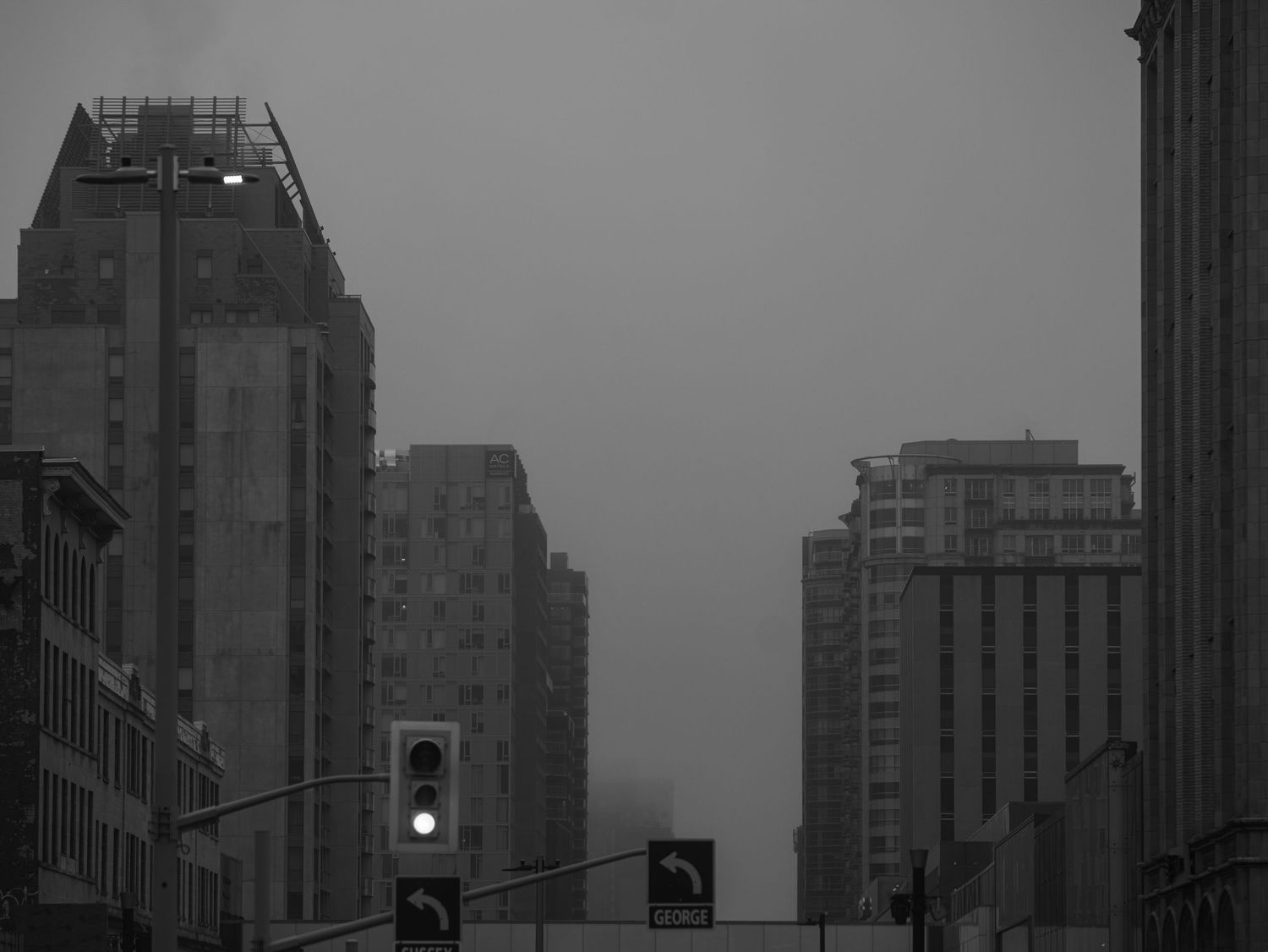 Dark moody black and white shot of tall city skyscrapers disappearing into fog at dusk.