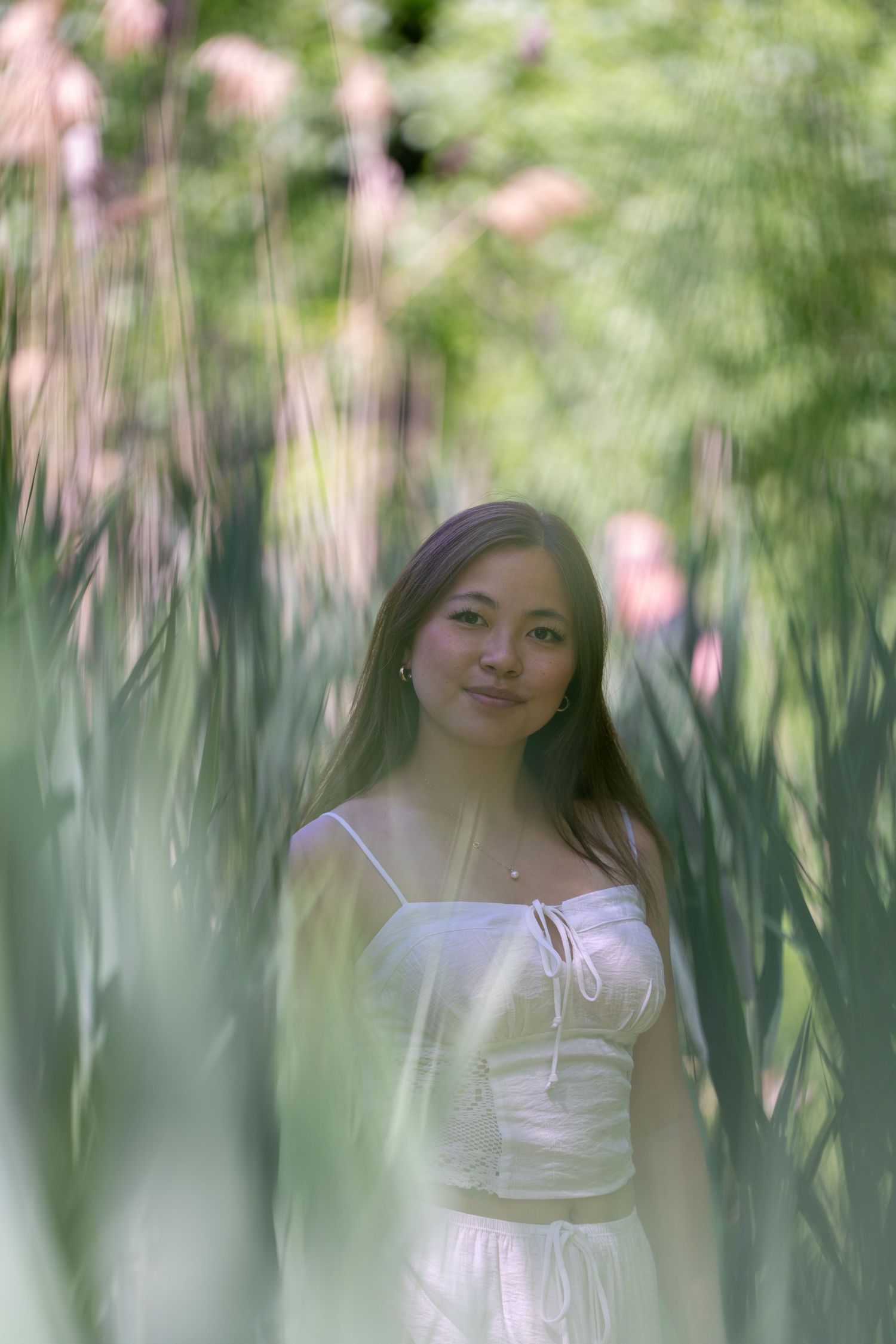 Young woman in a white dress standing among tall green plants in a sunlit garden.