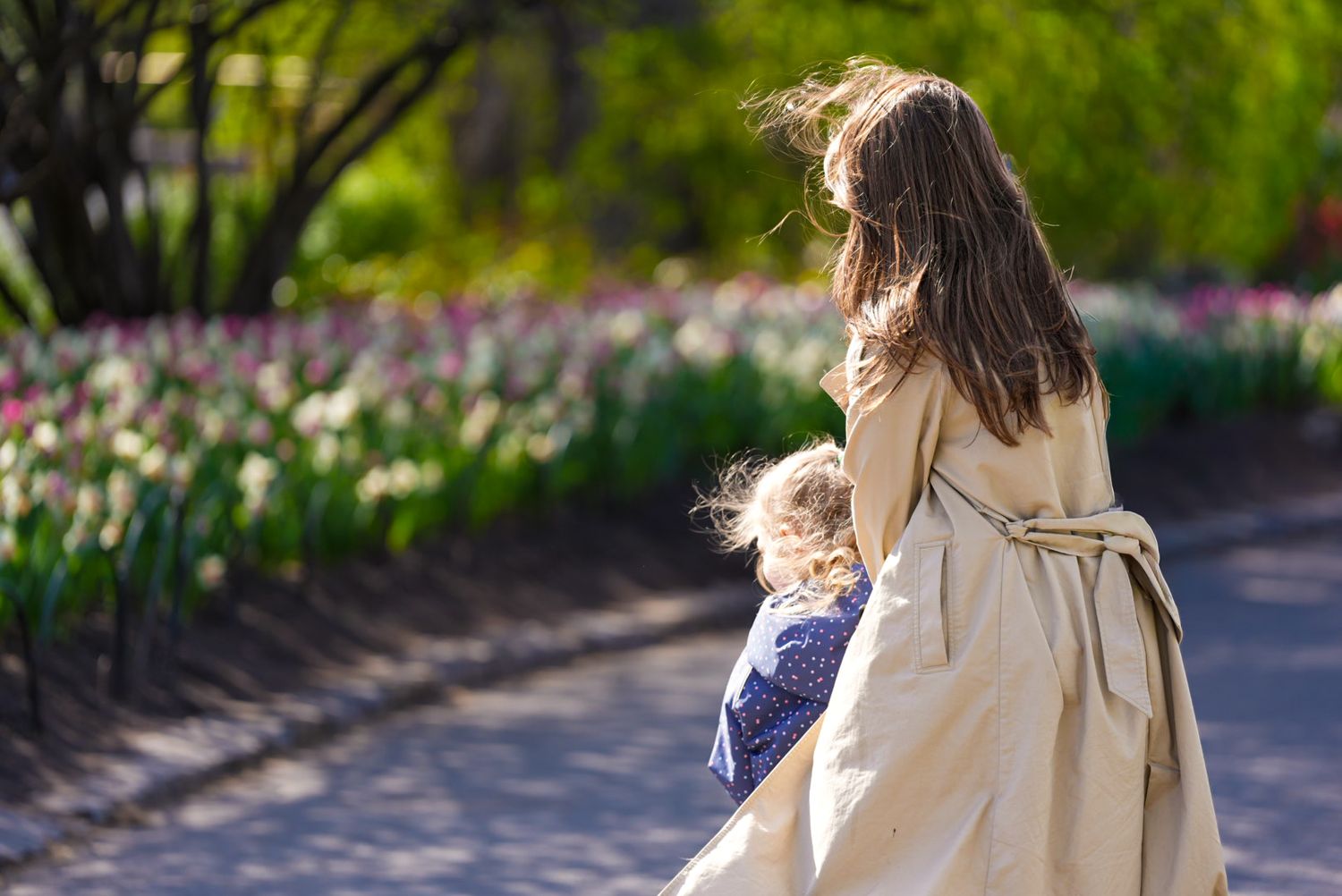 Woman in beige coat walking with child through a vibrant tulip garden in spring.