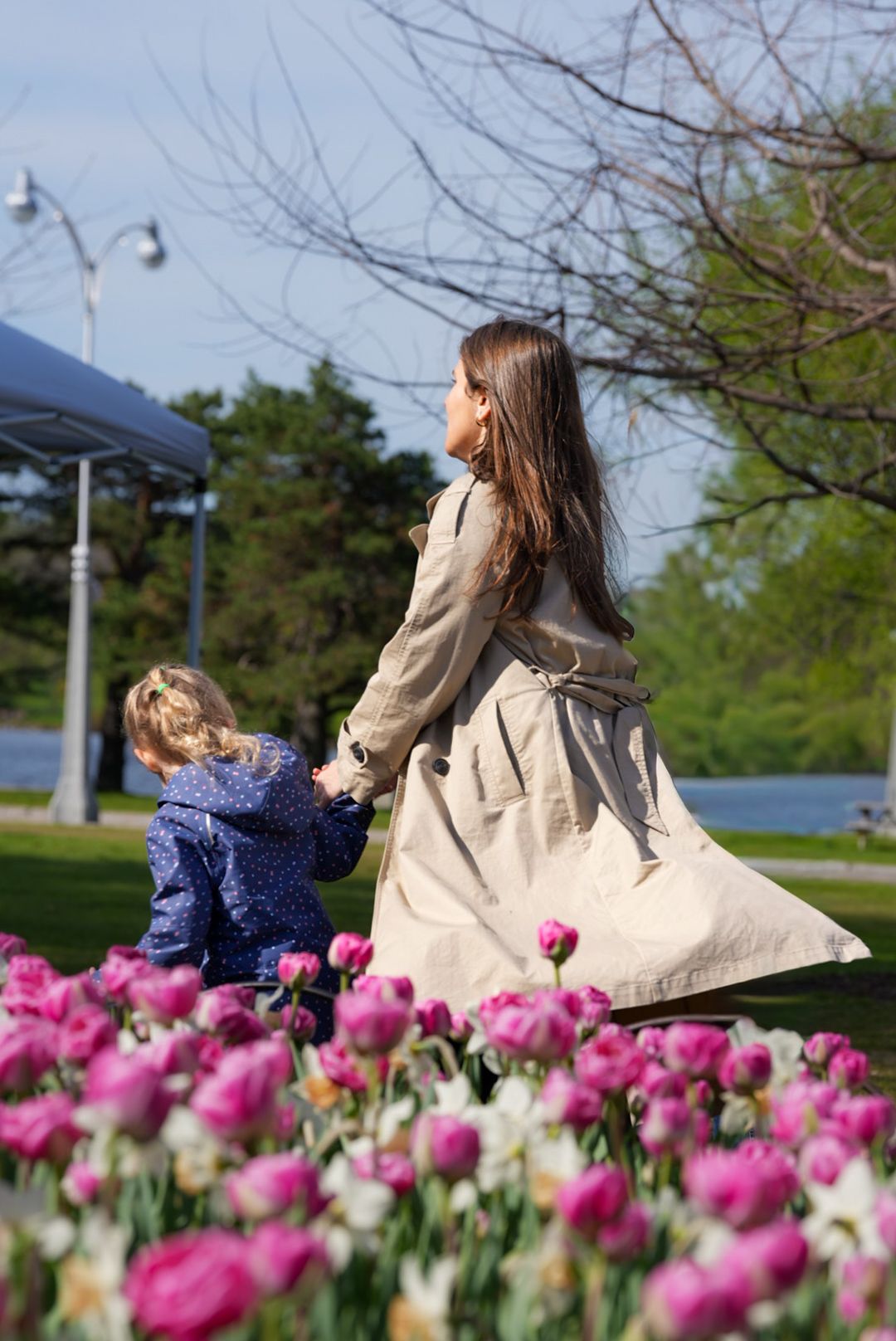 Mother and child holding hands among blooming pink tulips in a sunny park.