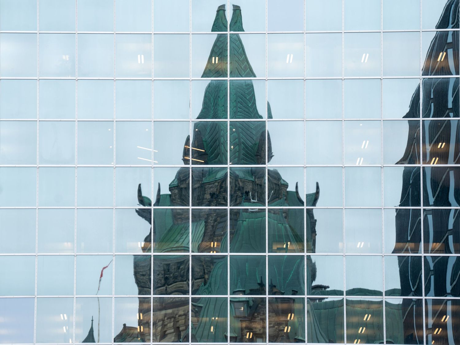 Reflection of a historic Gothic stone building tower mirrored in a modern glass curtain wall facade.