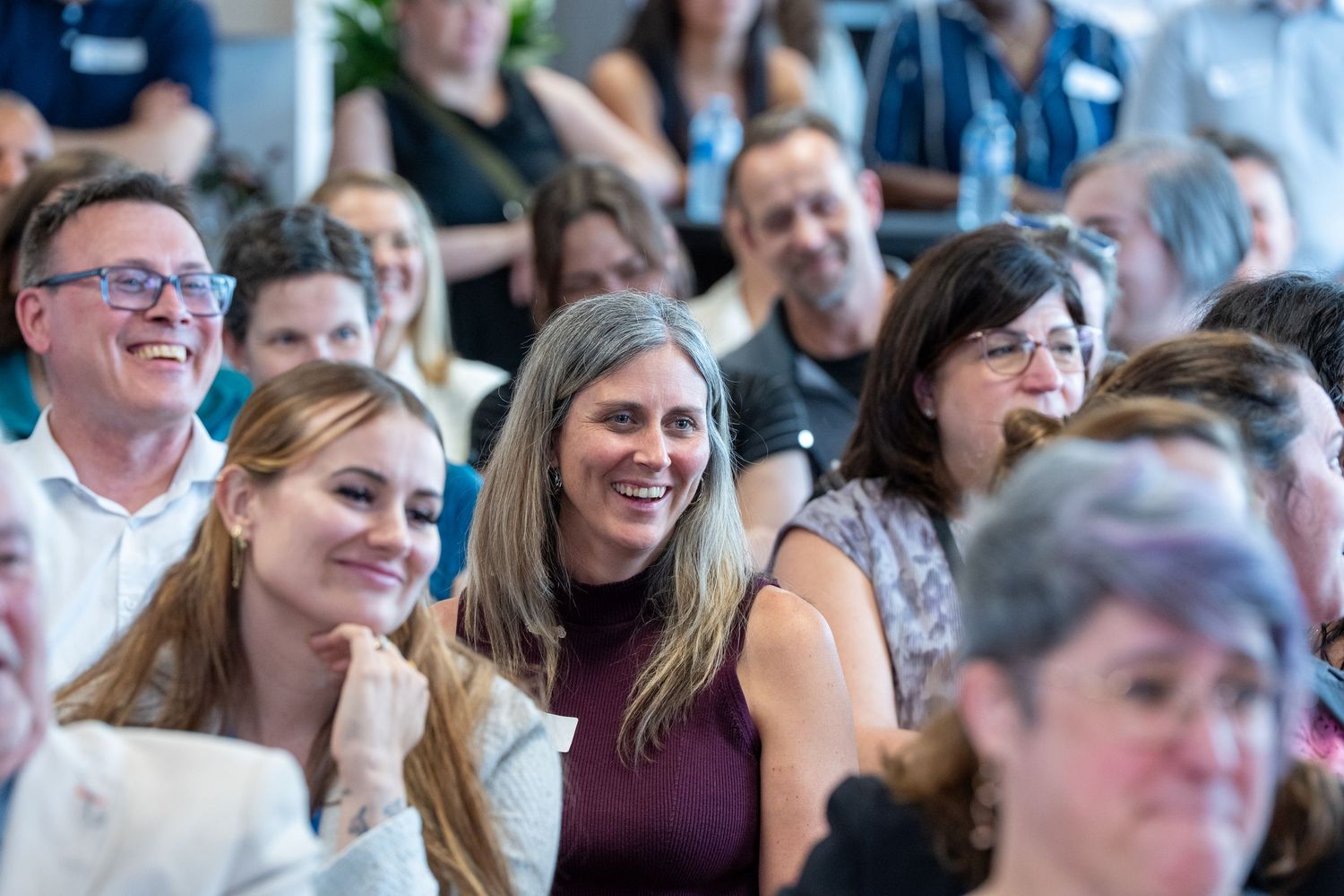 Diverse audience smiling and laughing at an indoor corporate or community event.
