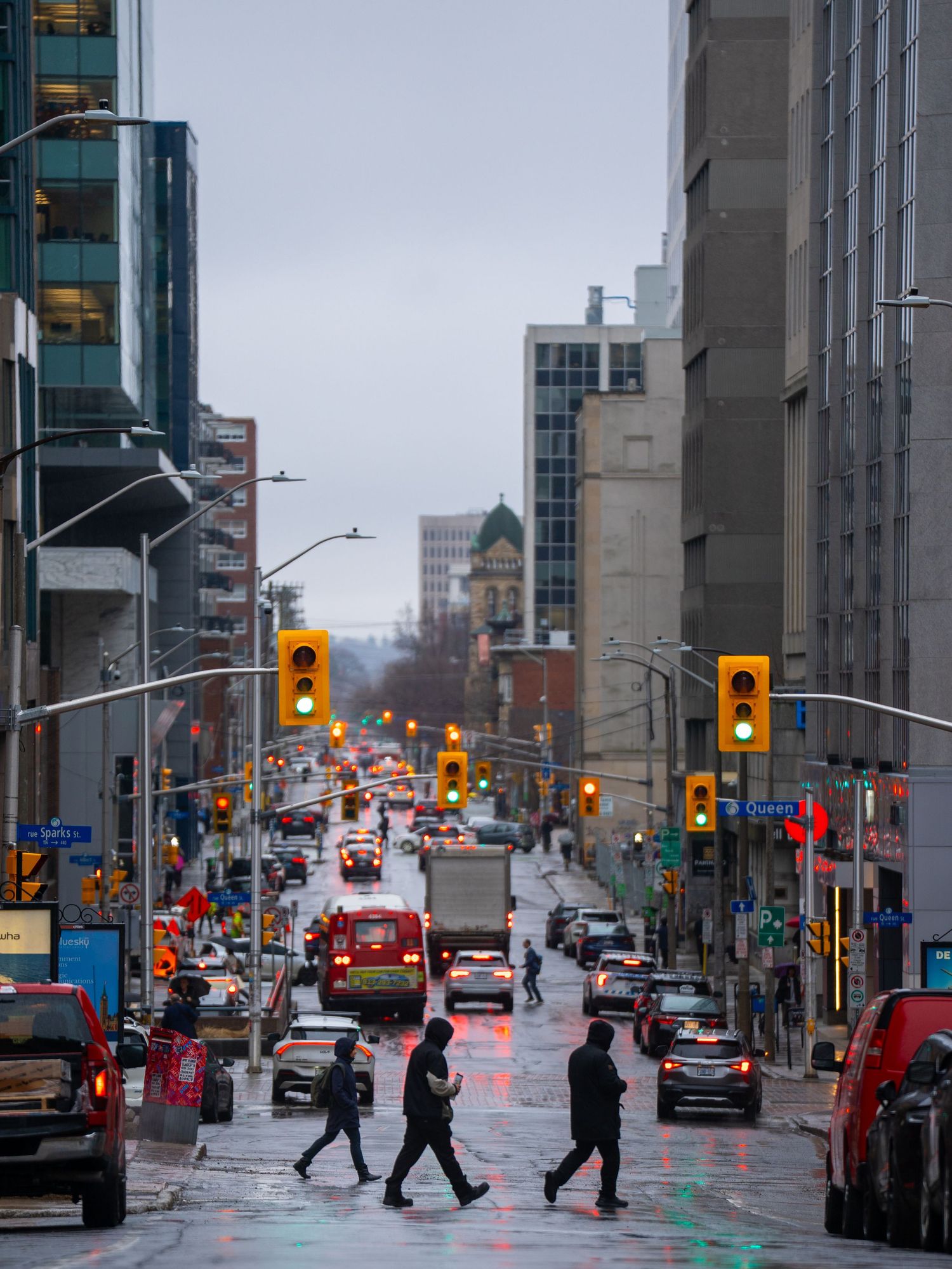 Rainy day urban street scene with pedestrians crossing a busy downtown intersection with glowing traffic lights.