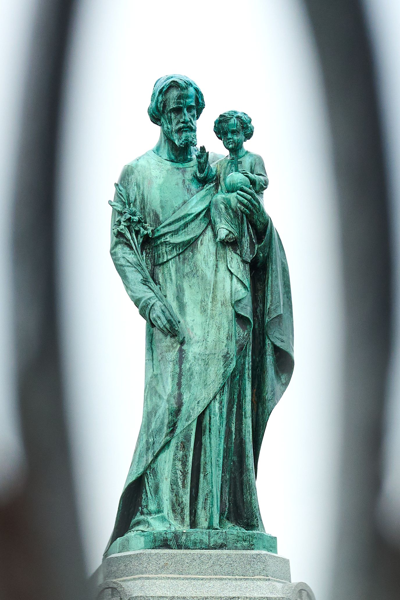 Close-up of a green patina bronze statue of Saint Joseph holding the Christ child on a pedestal.