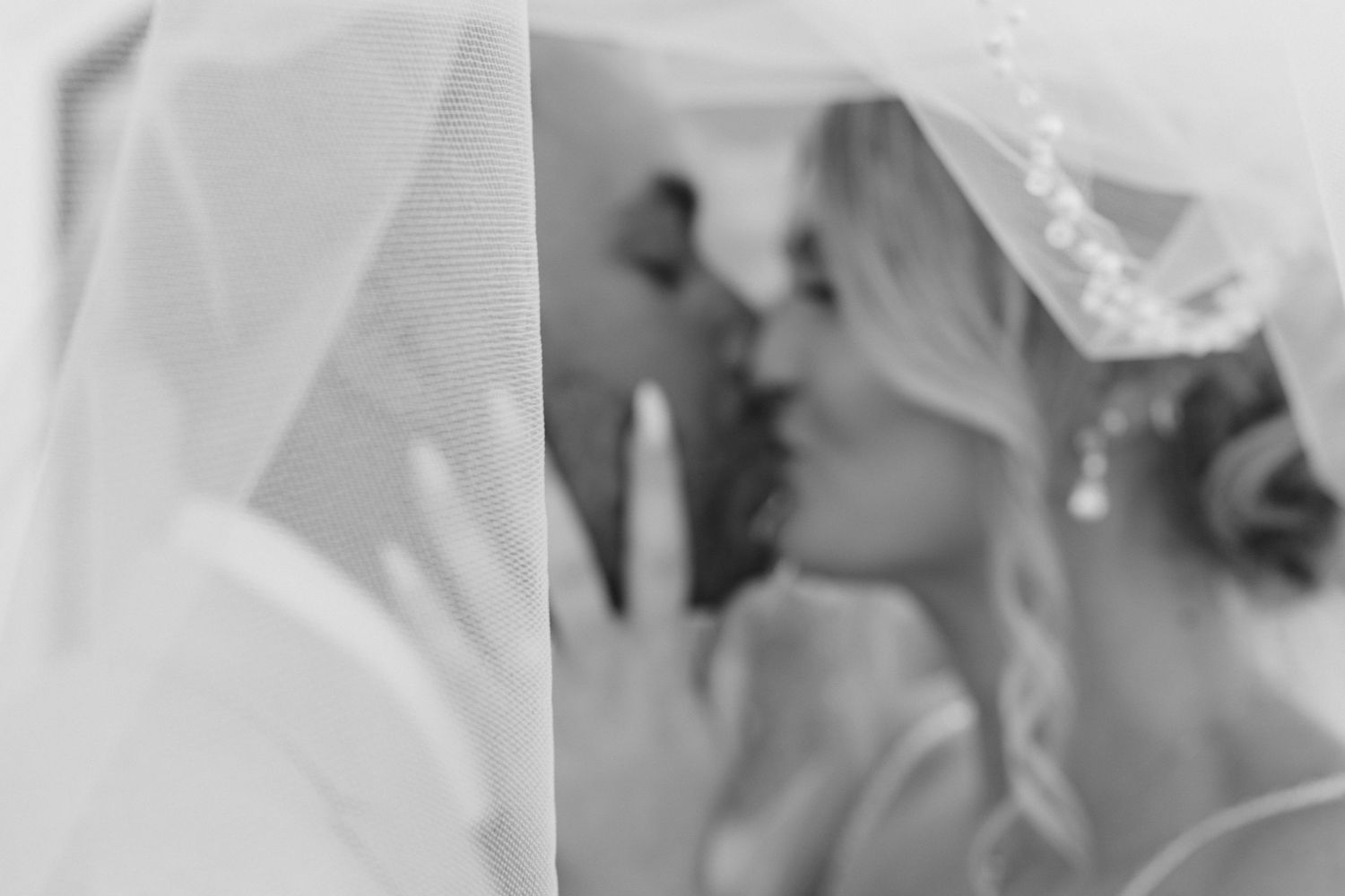 Black and white wedding photo of bride and groom kissing under a veil, capturing an intimate romantic moment.