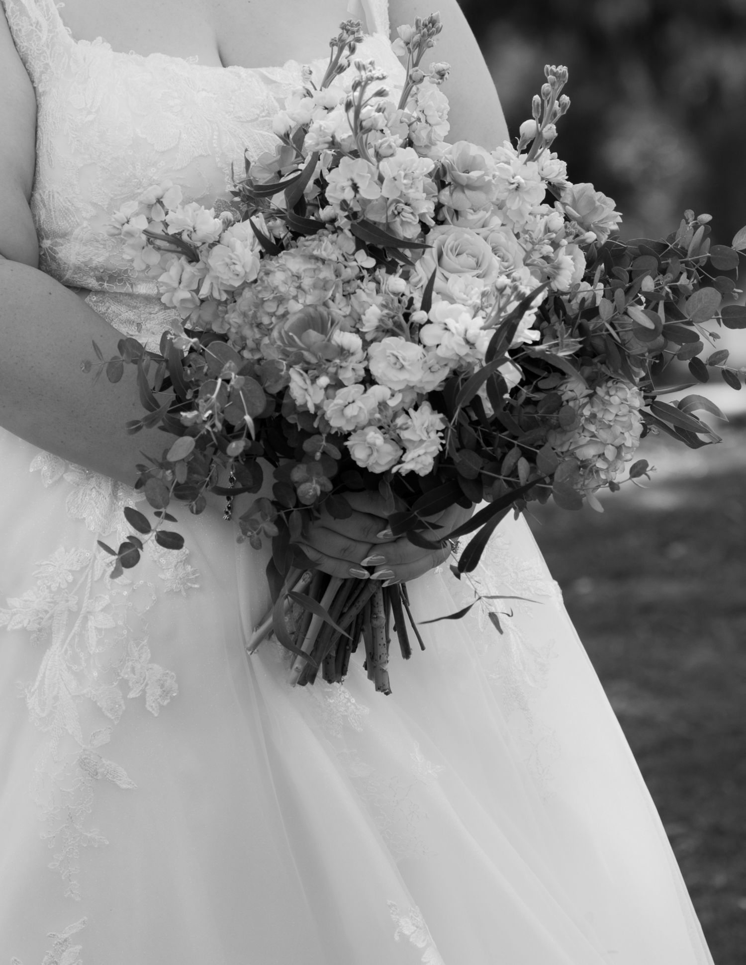 Black and white photo of a bride in lace gown holding a lush bouquet of roses and eucalyptus on her wedding day.