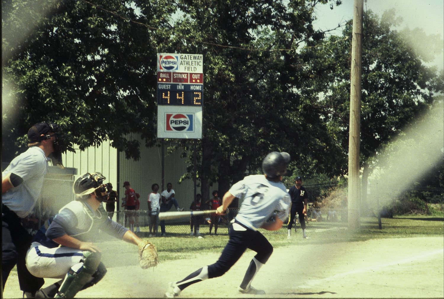 Baseball batter swinging at home plate with scoreboard and Pepsi sign in background.