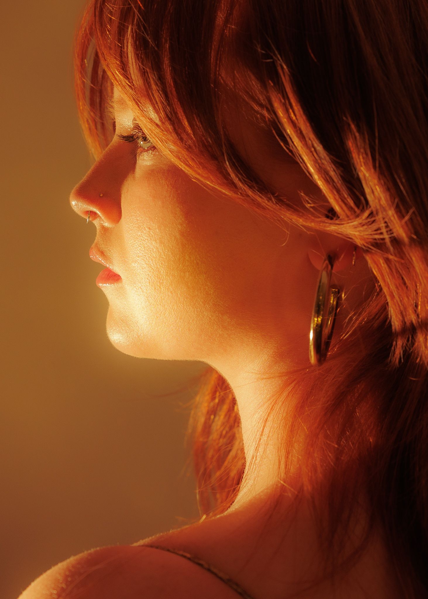 Profile portrait of a red-haired woman with hoop earrings in warm golden light.