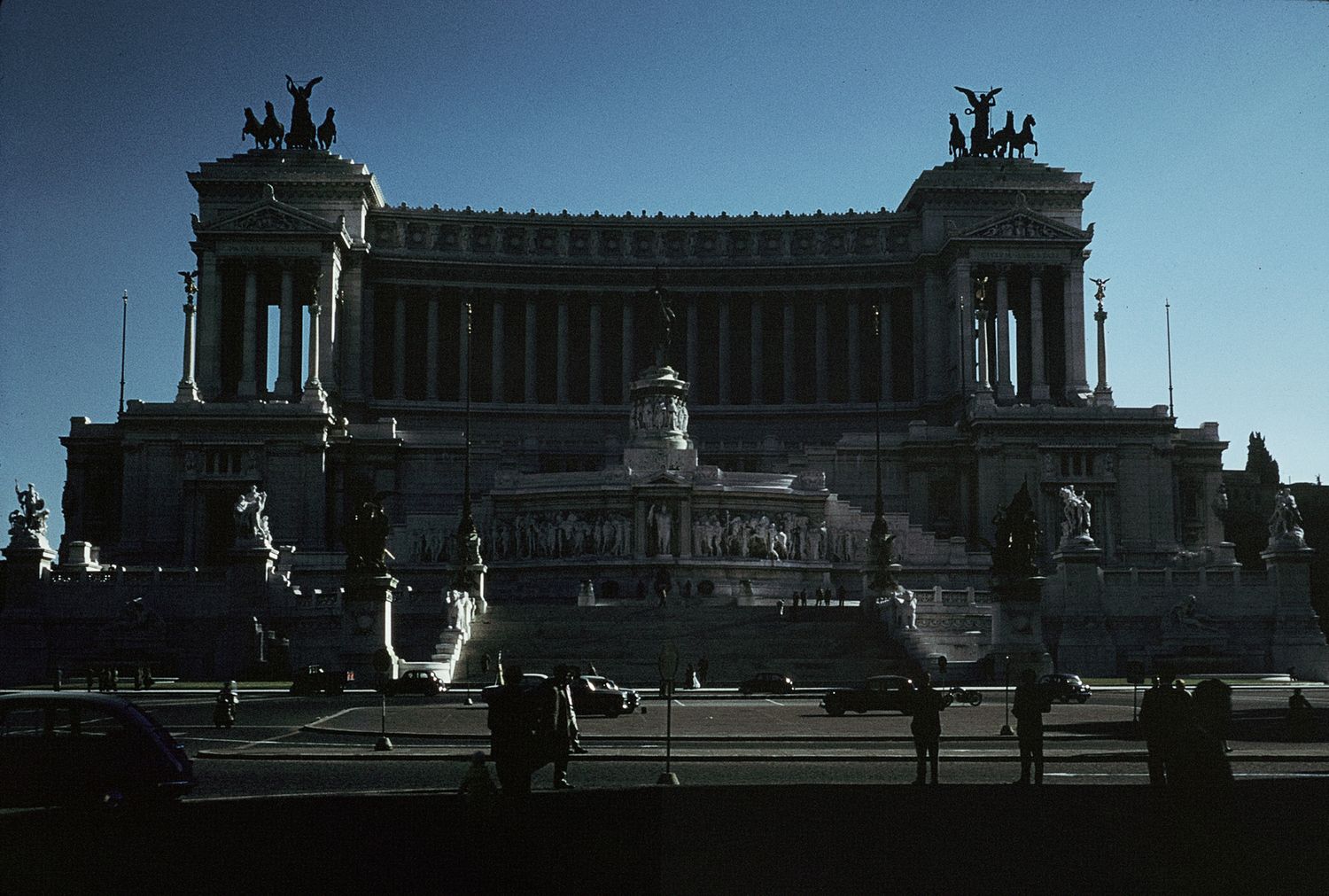 The Altare della Patria monument in Rome, Italy, photographed at dusk with silhouetted figures in the foreground.