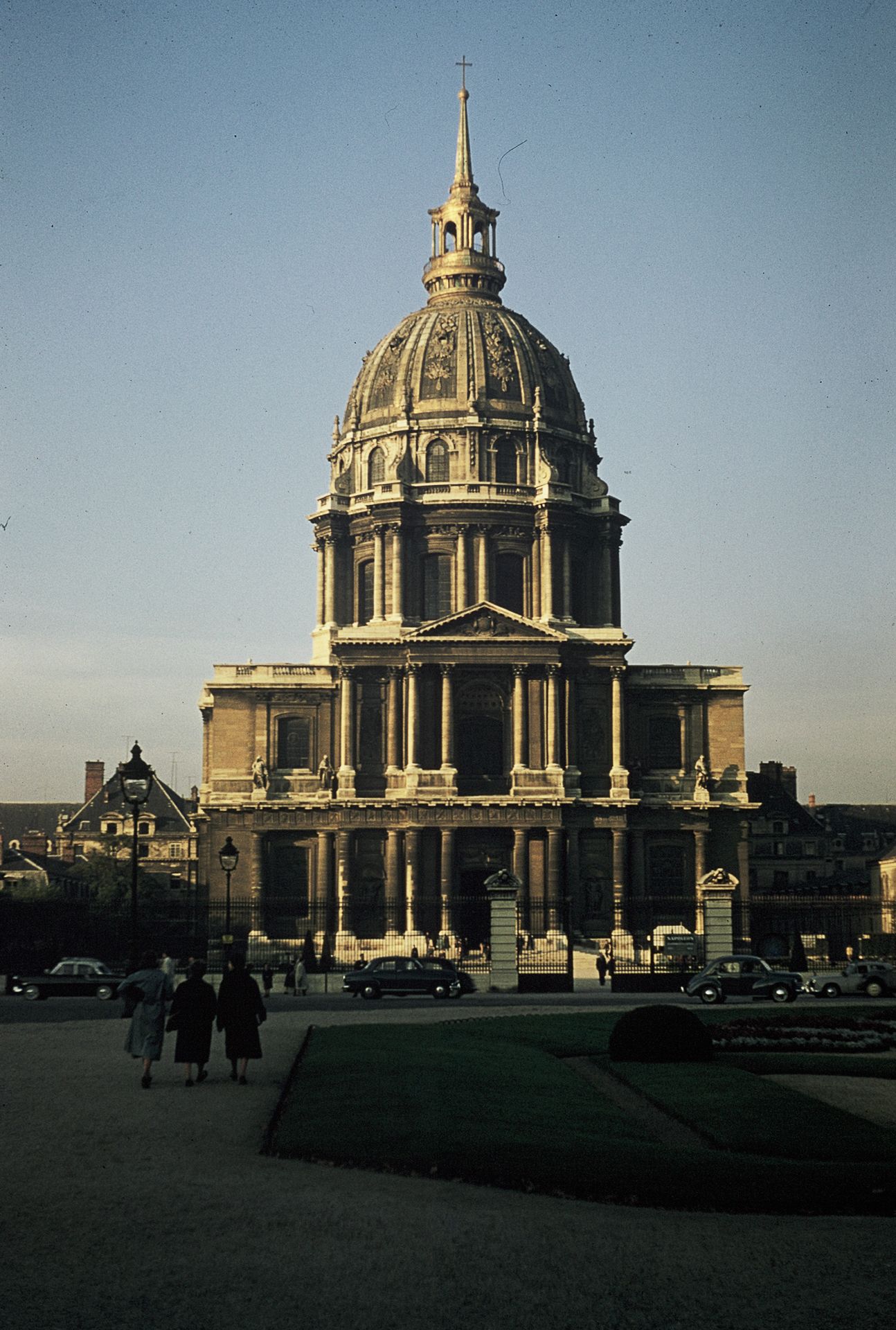 Les Invalides golden dome cathedral in Paris photographed at dusk with pedestrians in the foreground.