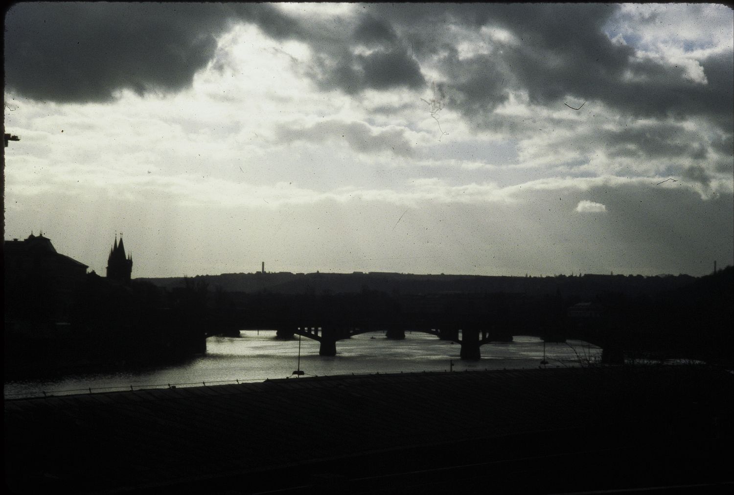 Dramatic silhouette of a bridge over a river at dusk with moody clouds and sunrays breaking through.