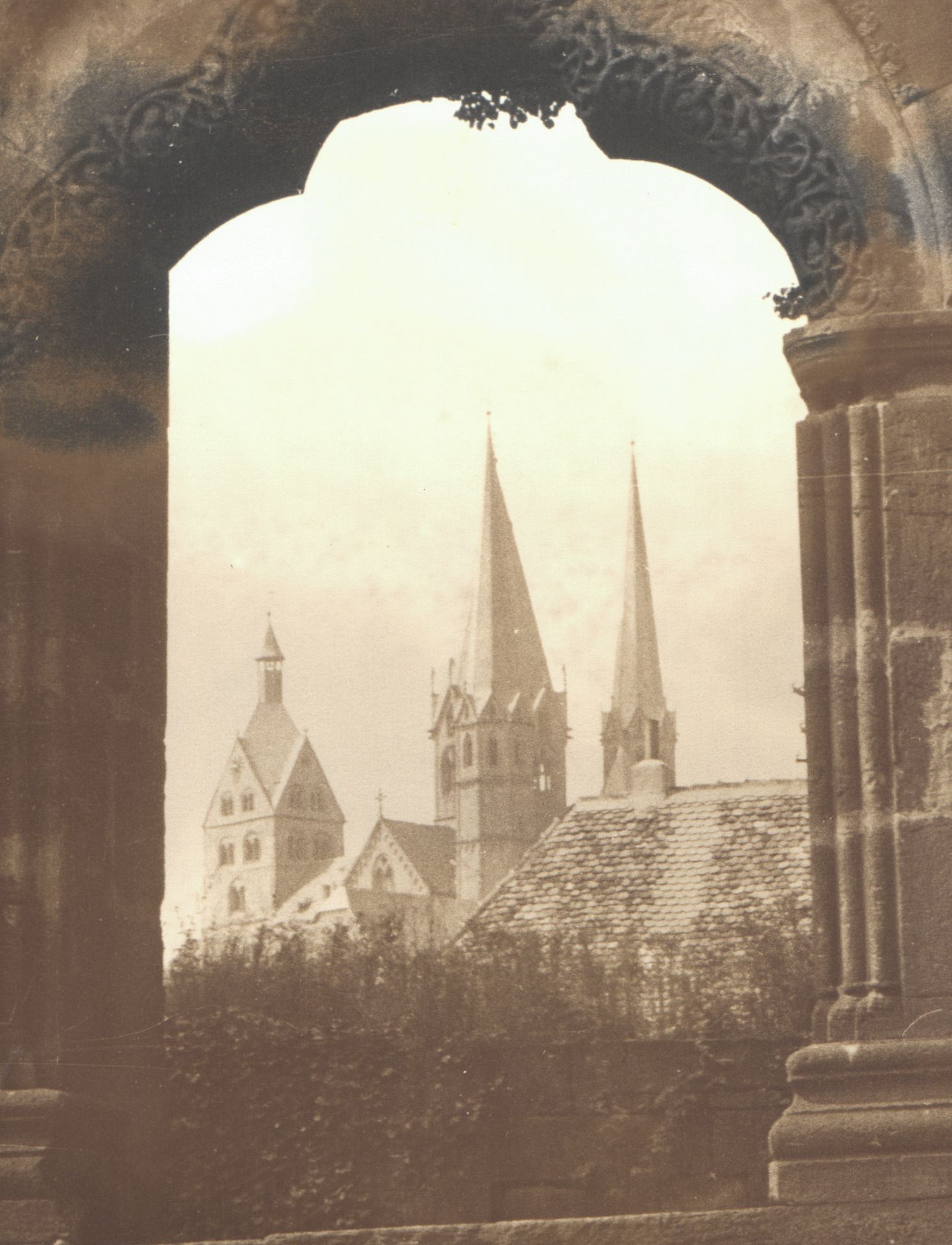 Sepia photograph of Gothic church spires viewed through a ornate stone archway in a historic European town.