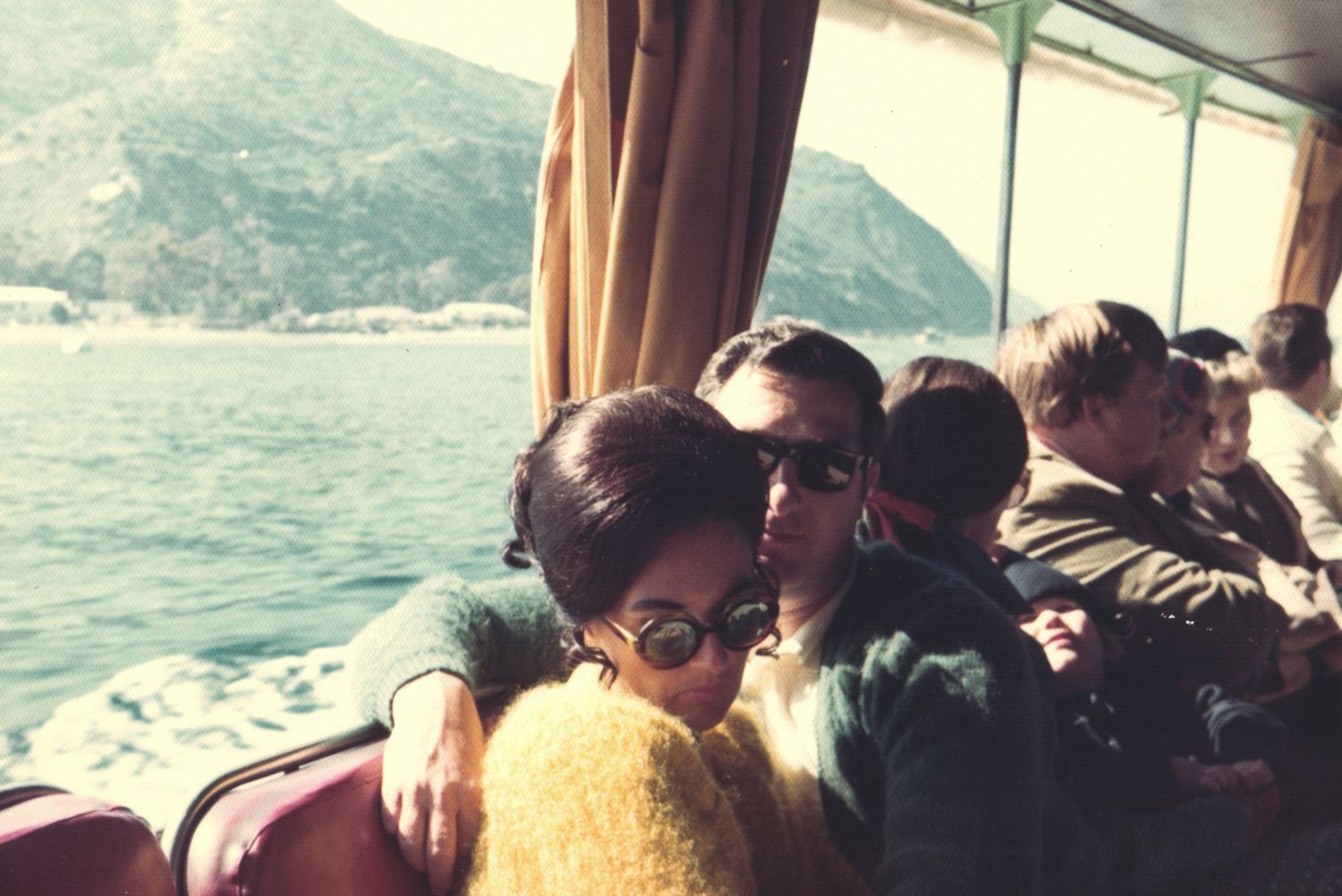 Couple embracing on a boat with mountain and water views in a vintage retro photo.