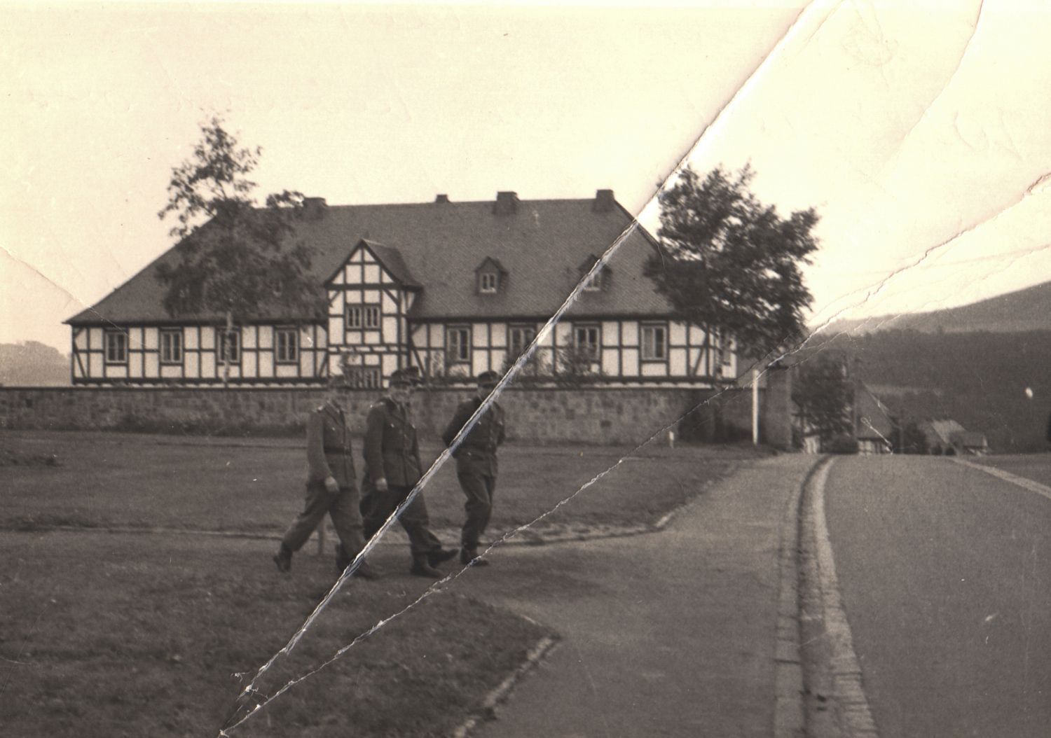Vintage black and white photo of a half-timbered German farmhouse with two people walking along a rural road.
