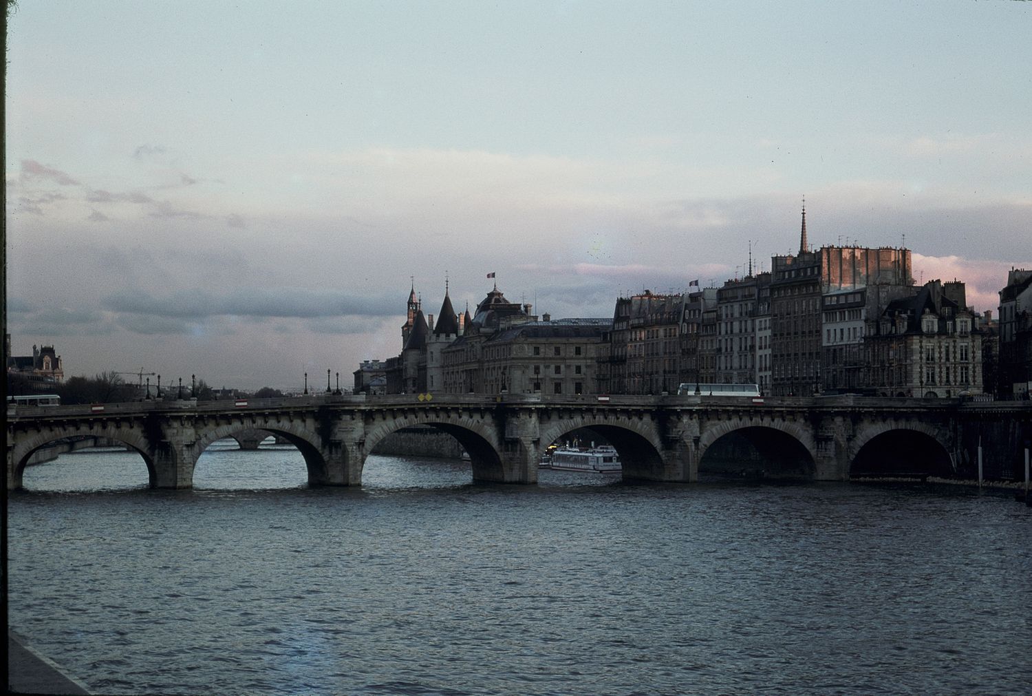 Historic stone bridge spanning the Seine River in Paris at dusk with city buildings behind.