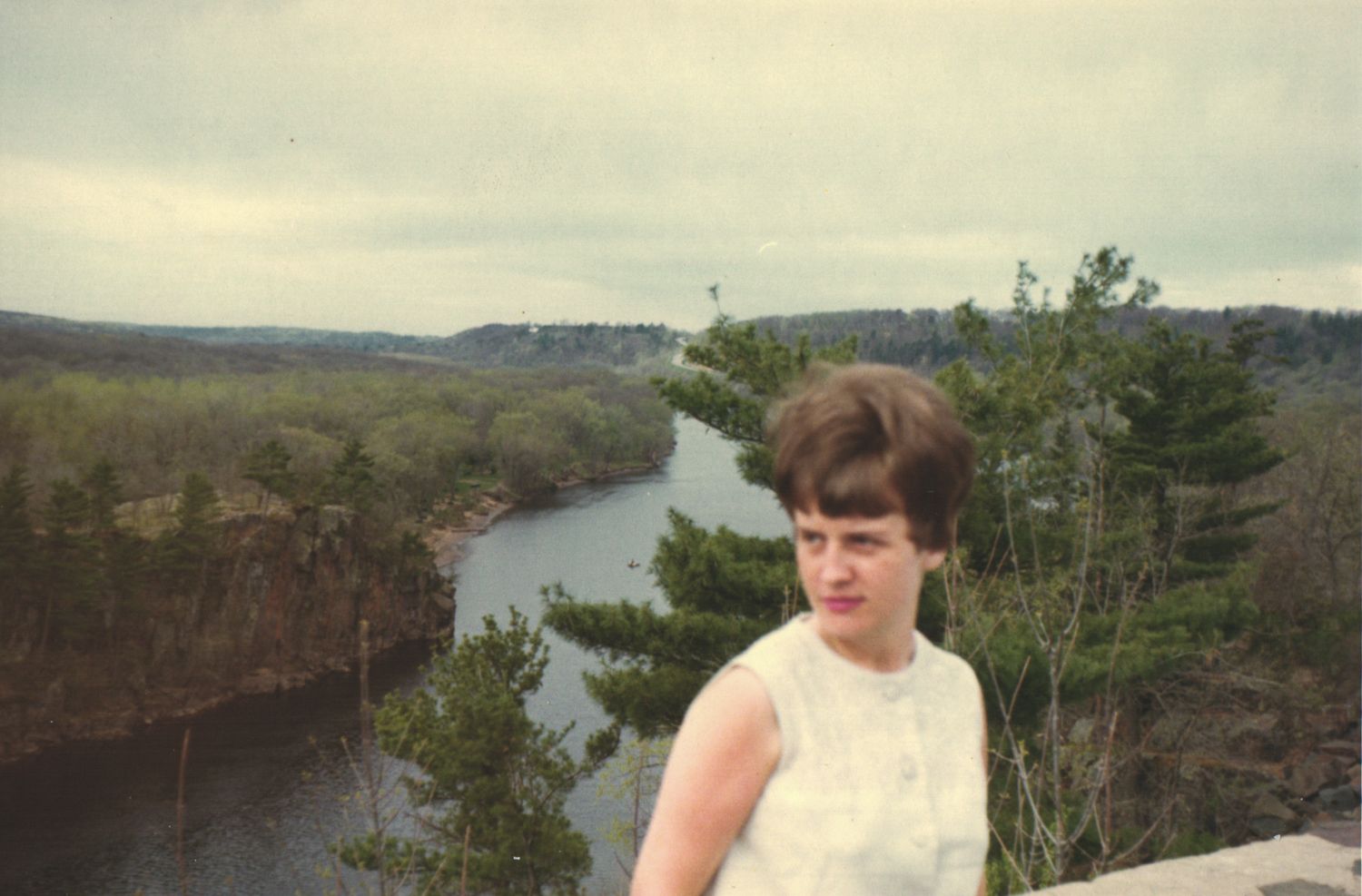 Young woman in white dress standing at scenic overlook above a winding river valley.