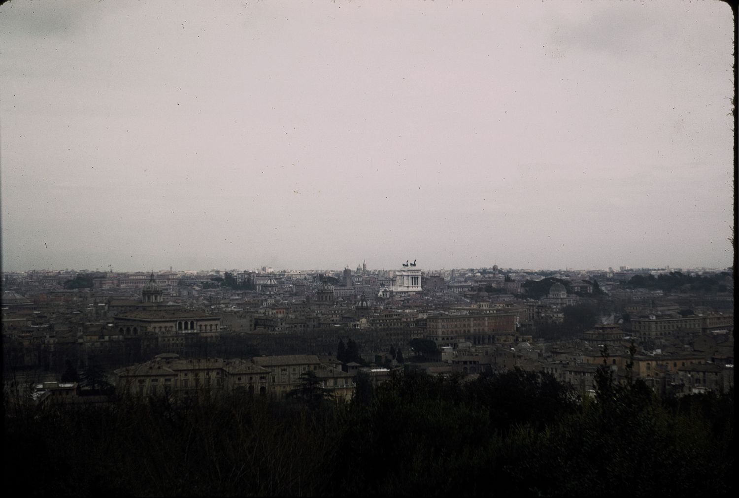 Panoramic aerial view of Rome's historic cityline with ancient ruins and domed buildings under overcast skies.