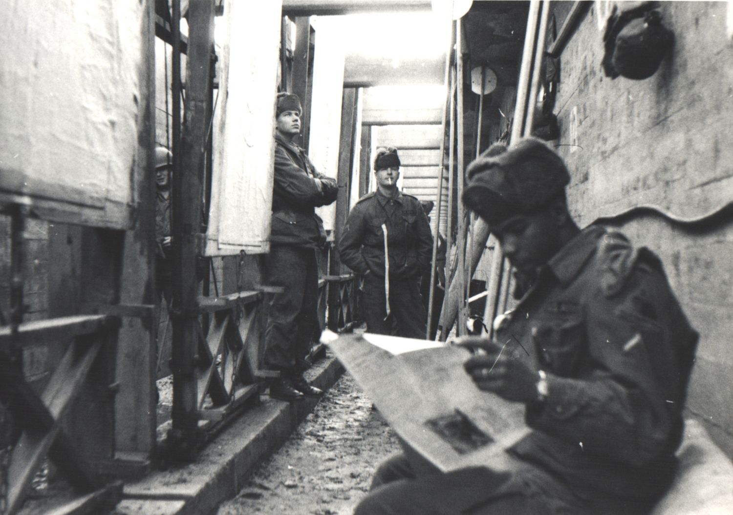 Black and white photo of soldiers reading between train cars in a narrow corridor.