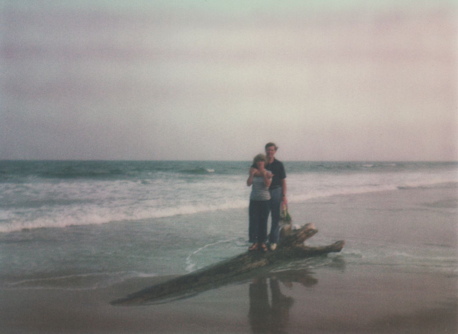 Couple embracing on driftwood at a misty beach with ocean waves in the background.