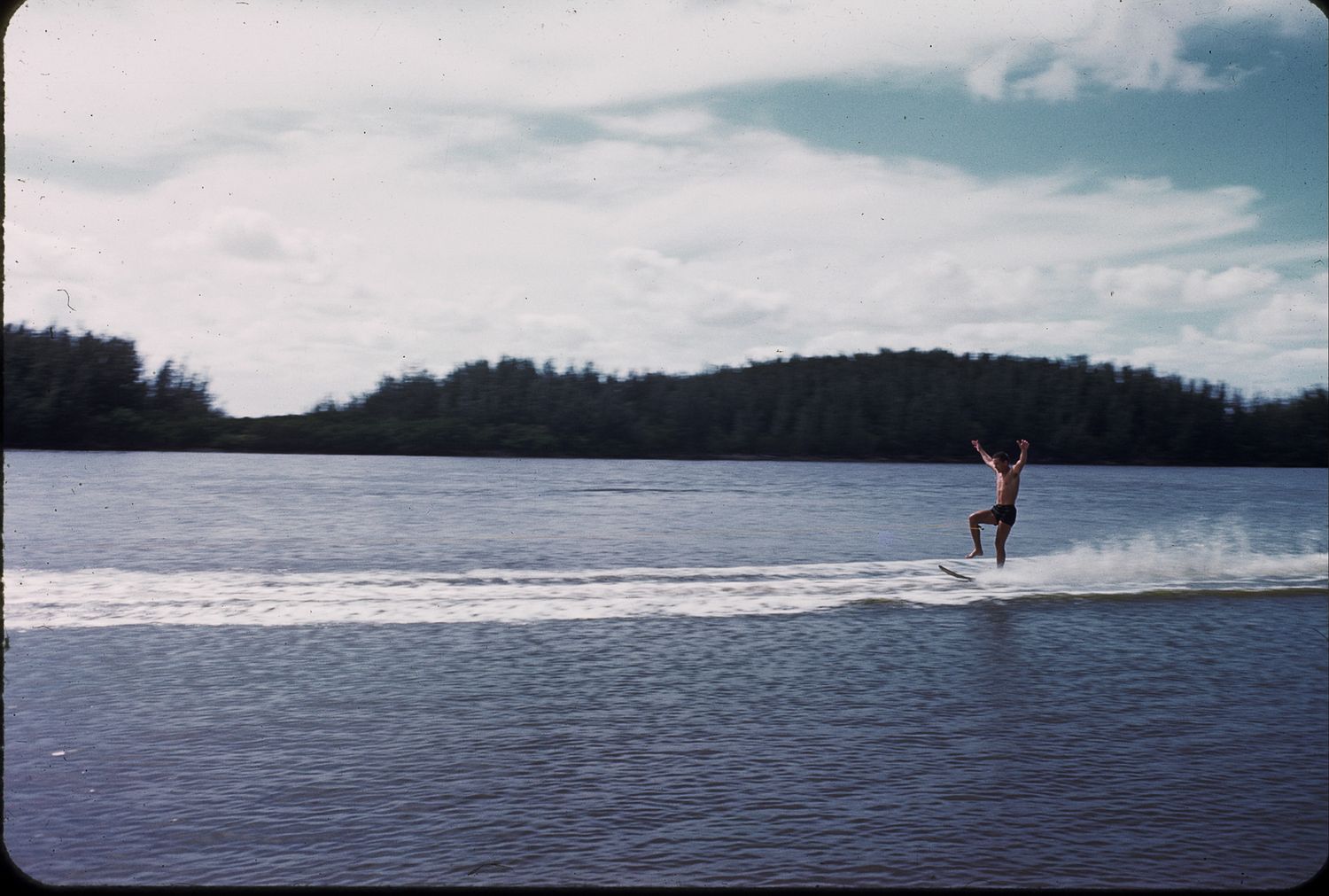 Water skier gliding across a calm tropical lake with lush green forest in the background.
