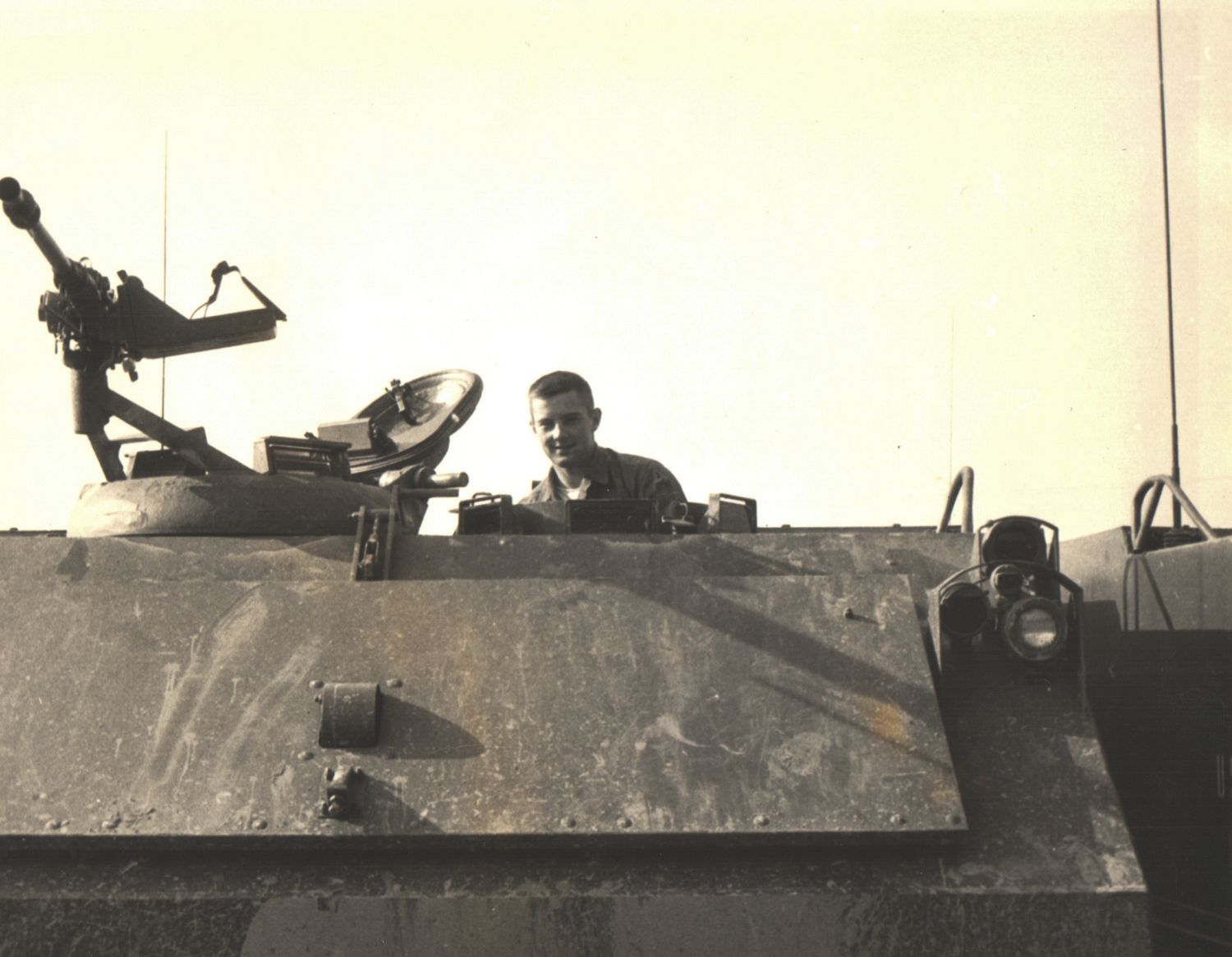 Soldier smiling from the hatch of a military tank or armored vehicle in a vintage black and white photo.