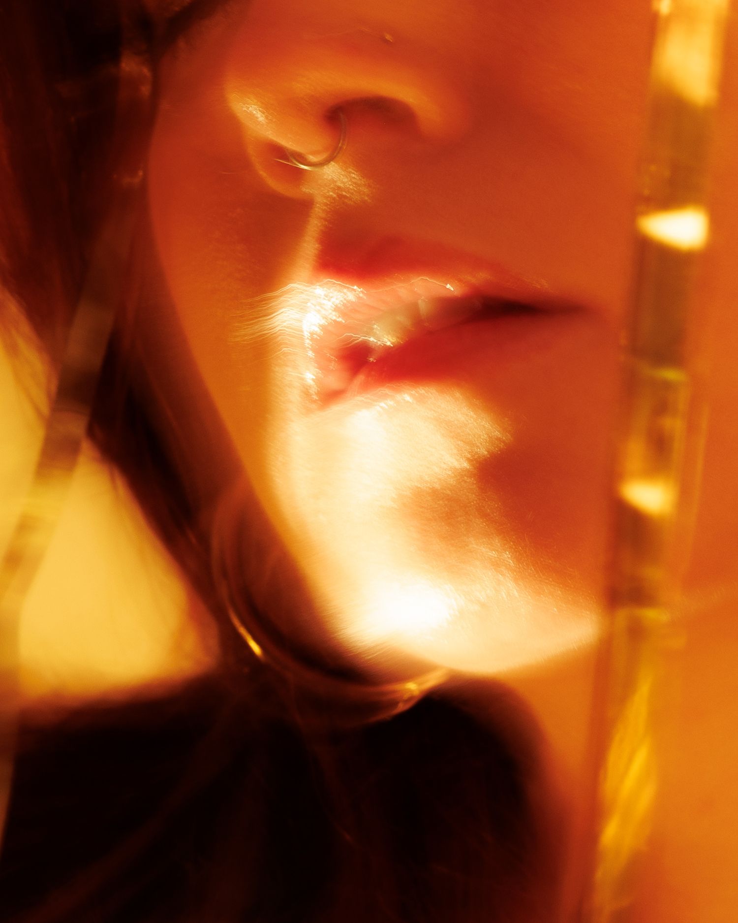 Close-up portrait of a woman bathed in warm golden orange light, highlighting her lips and nose with artistic blur.