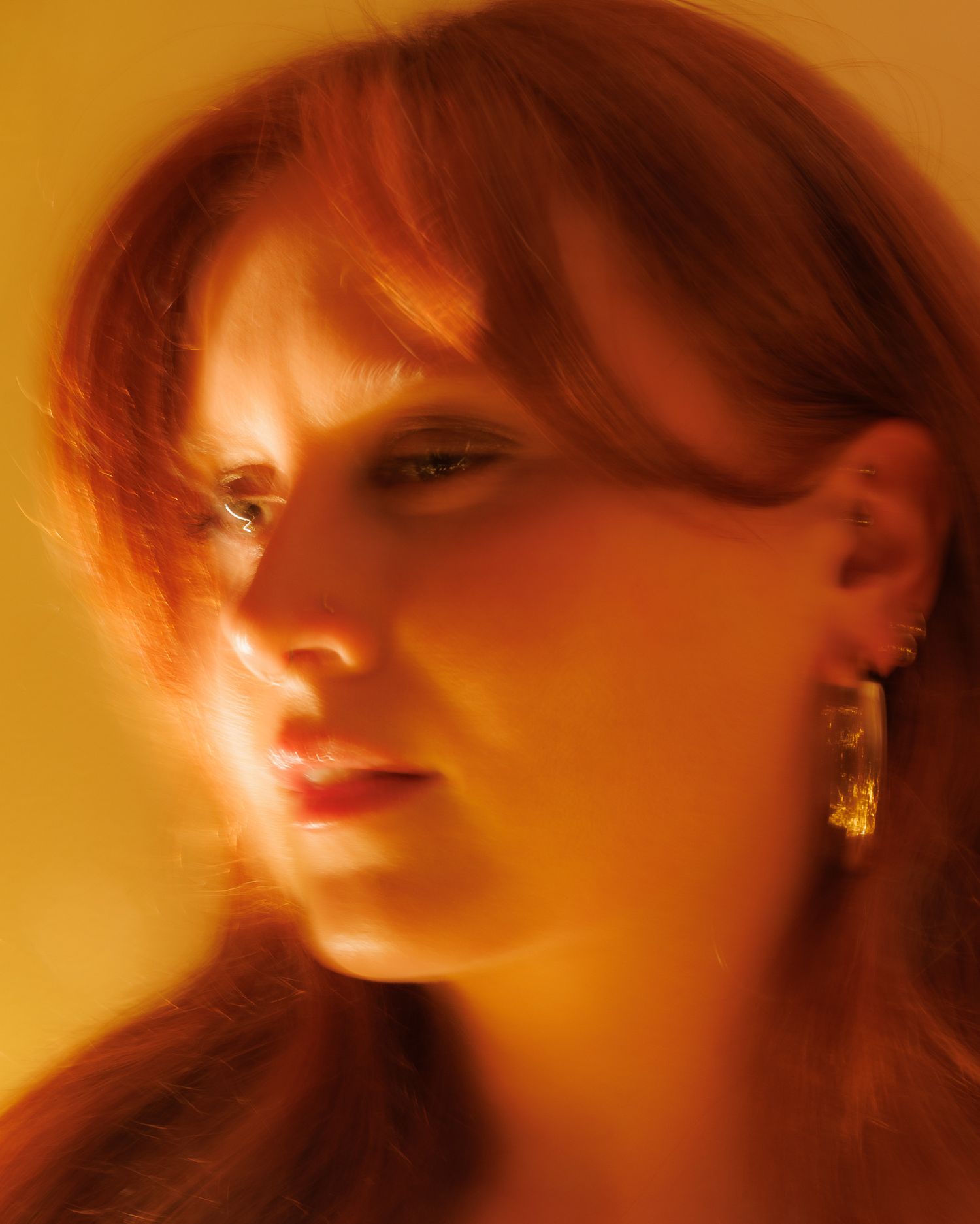 Close-up portrait of redhead woman with gold earrings in warm golden orange dramatic lighting.