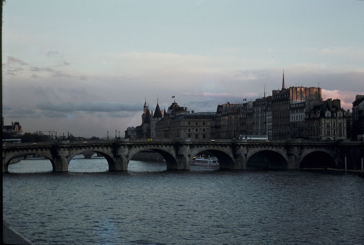 Historic Pont Neuf bridge spanning the Seine River in Paris at dusk, with classic Haussmann buildings lining the riverbank.