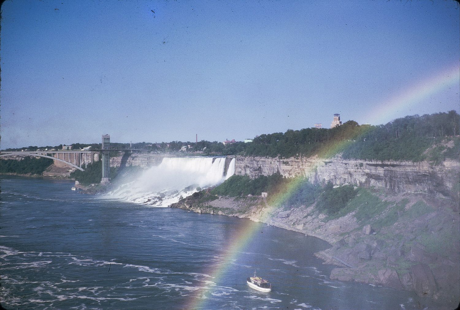Niagara Falls with a vibrant rainbow arching over the misty cascading waterfall and tour boat.