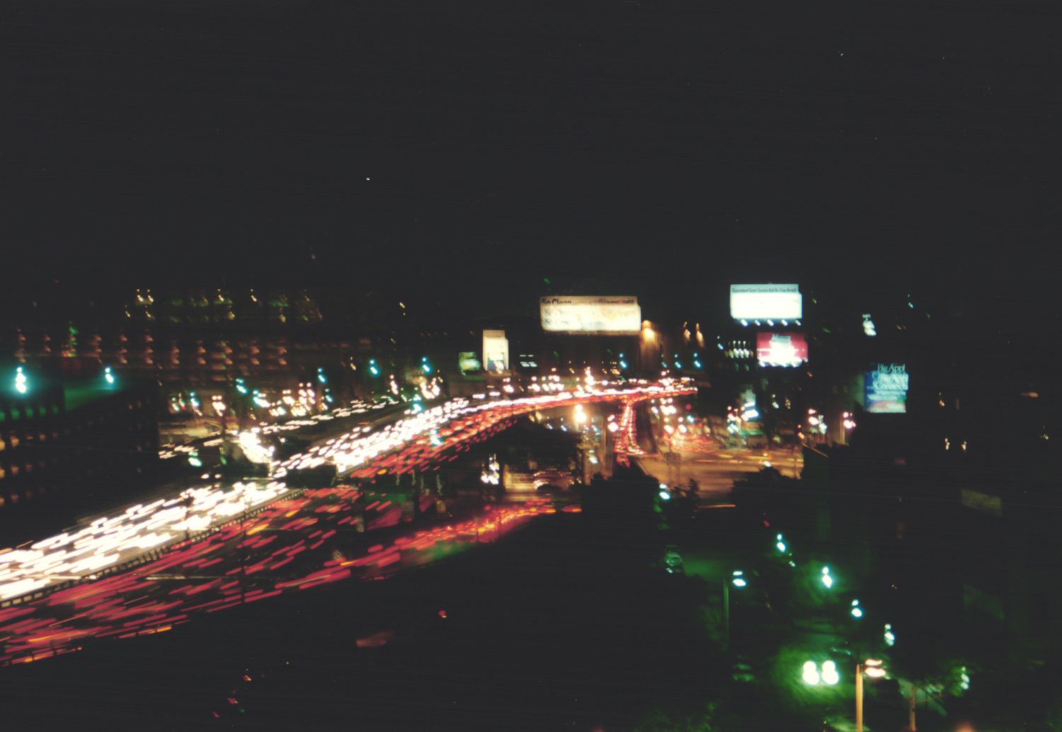 Aerial night view of busy city highway with light trails from traffic and illuminated billboards.