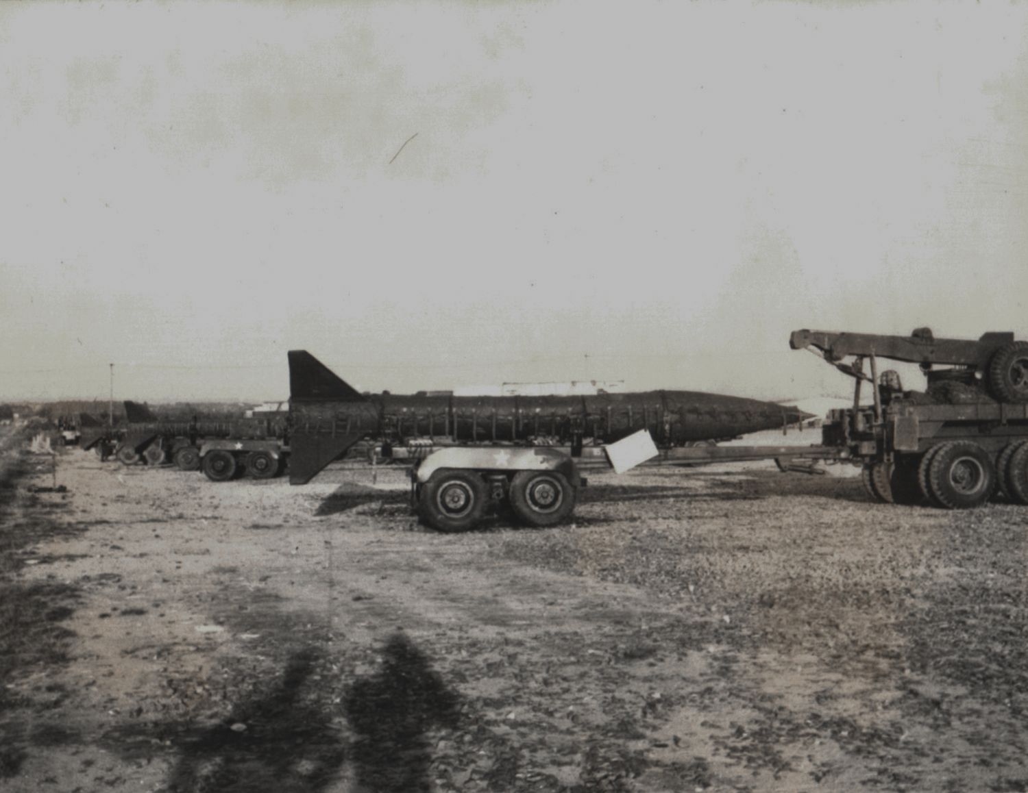 Vintage black and white photo of a military missile on a transport trailer in an open field.
