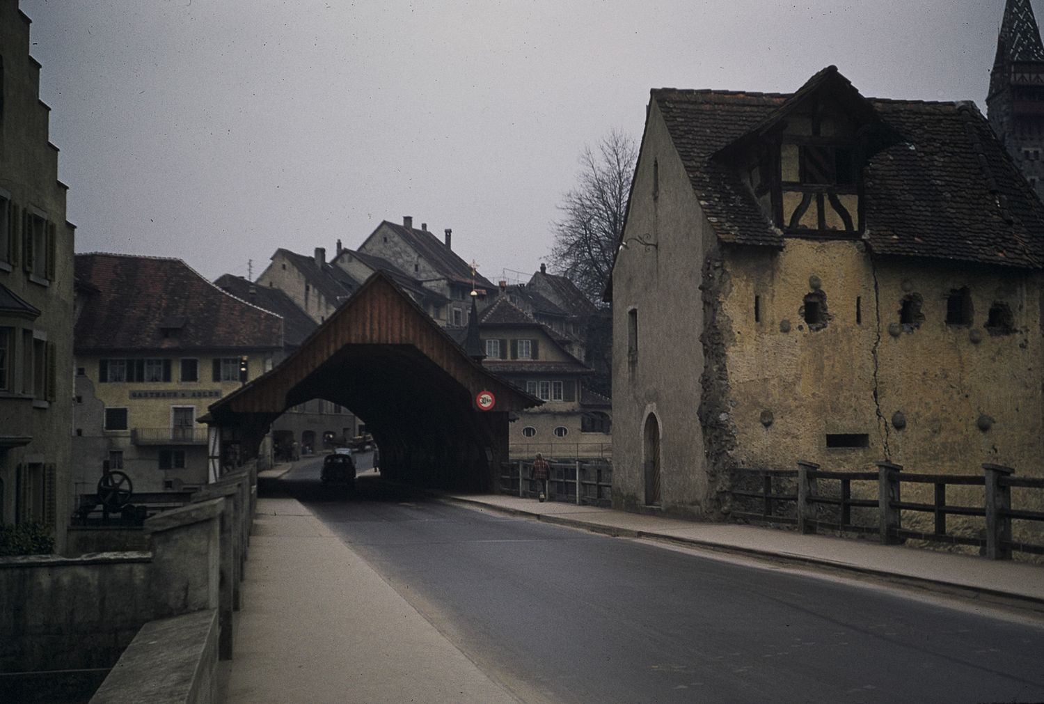 Medieval covered wooden bridge with red stop sign leads into a historic European village street.