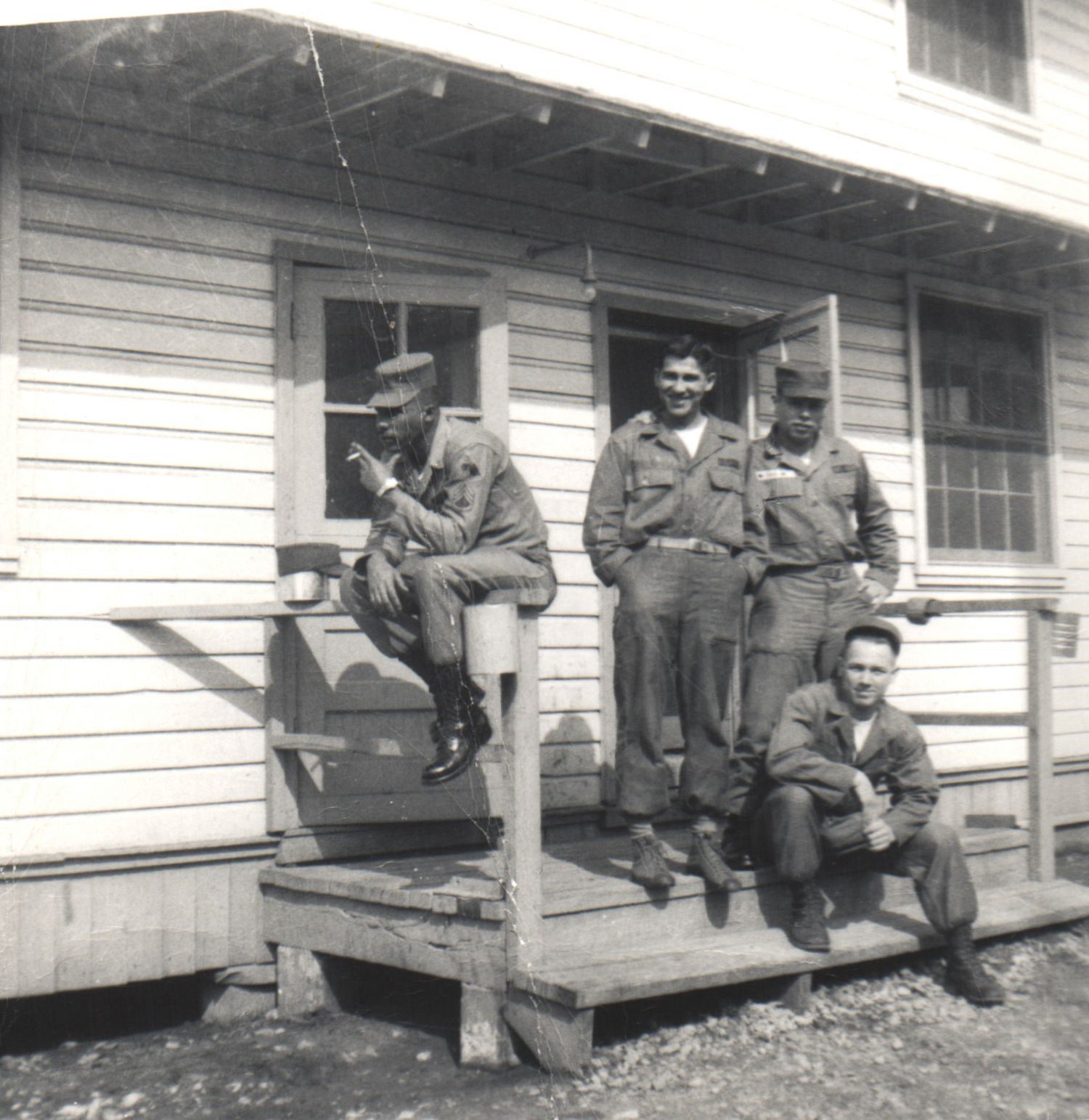 Four soldiers in military uniforms posing on a wooden porch of a white clapboard building.