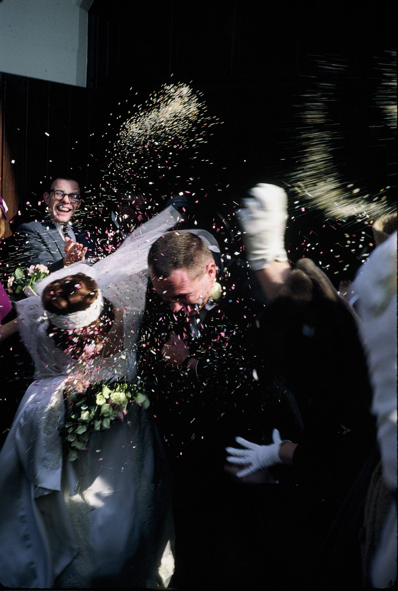 Wedding couple showered with confetti and rice outside church entrance with guests celebrating.