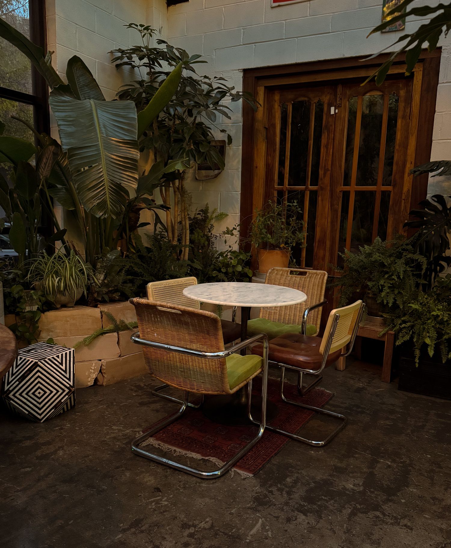 SAINT JAMES PHOTO- Cozy outdoor patio with wicker chairs, round table, and lush tropical plants.