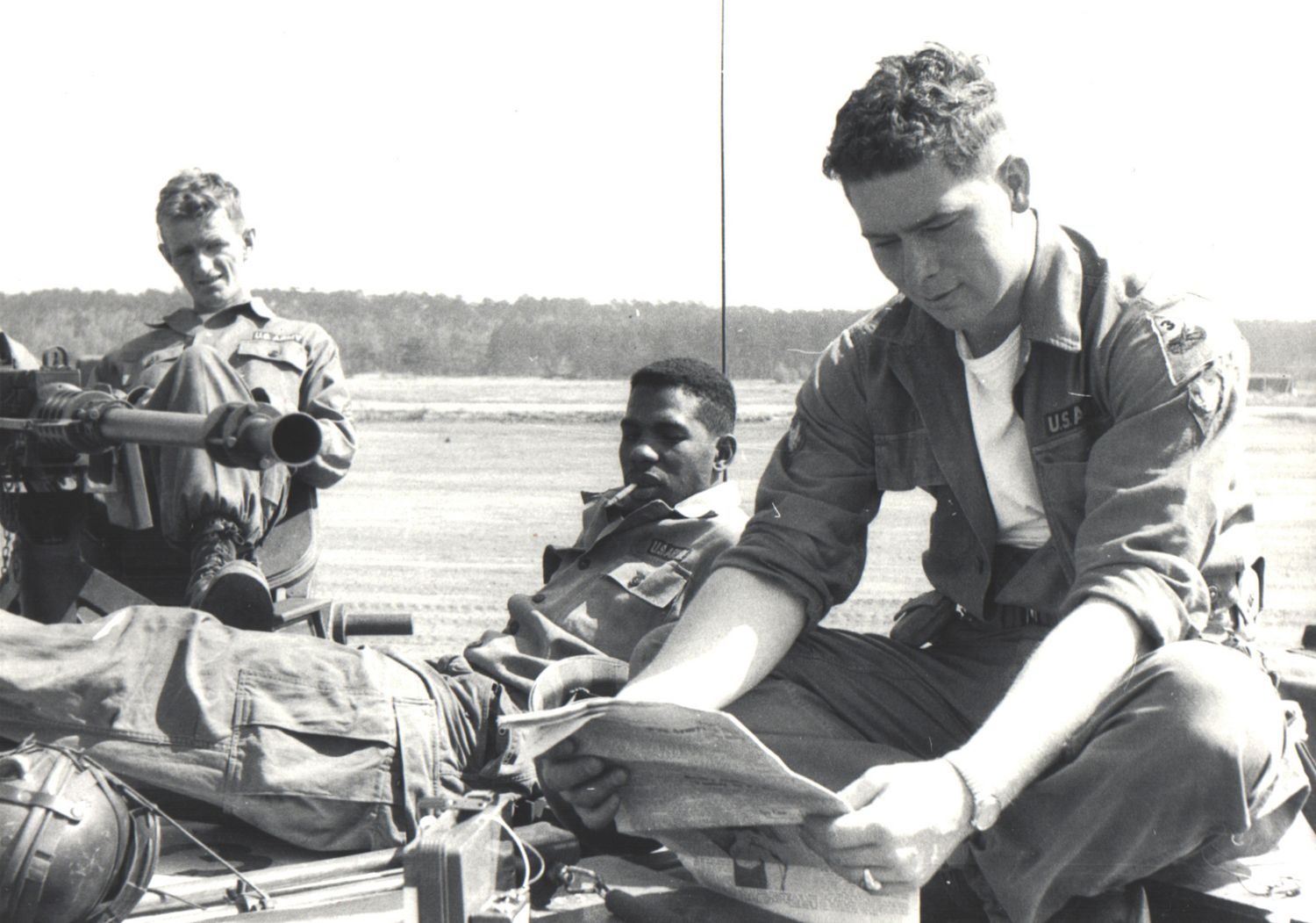 Three soldiers in military gear rest outdoors in a black and white vintage photograph.