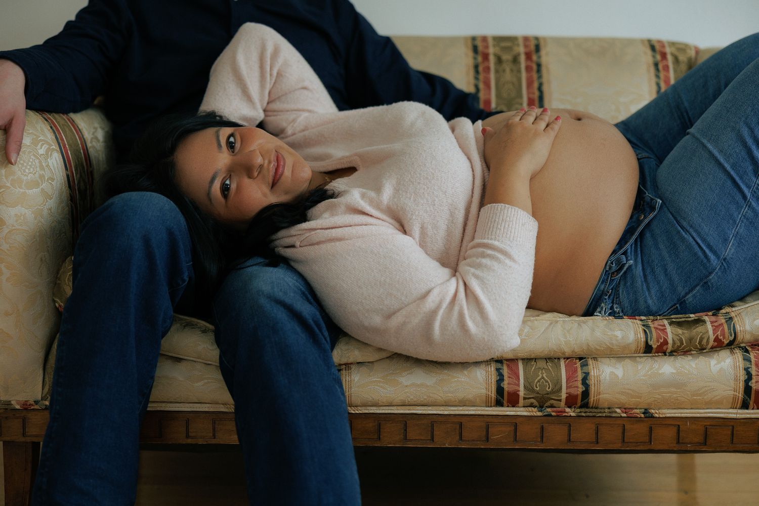 SAINT JAMES PHOTO- Pregnant woman rests on a vintage sofa beside her partner indoors.