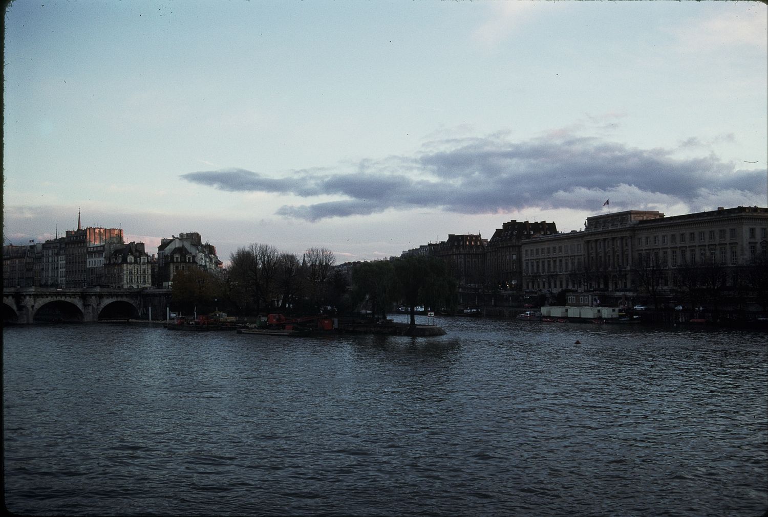 Scenic view of the Seine River in Paris at dusk with a bridge and city buildings along the bank.