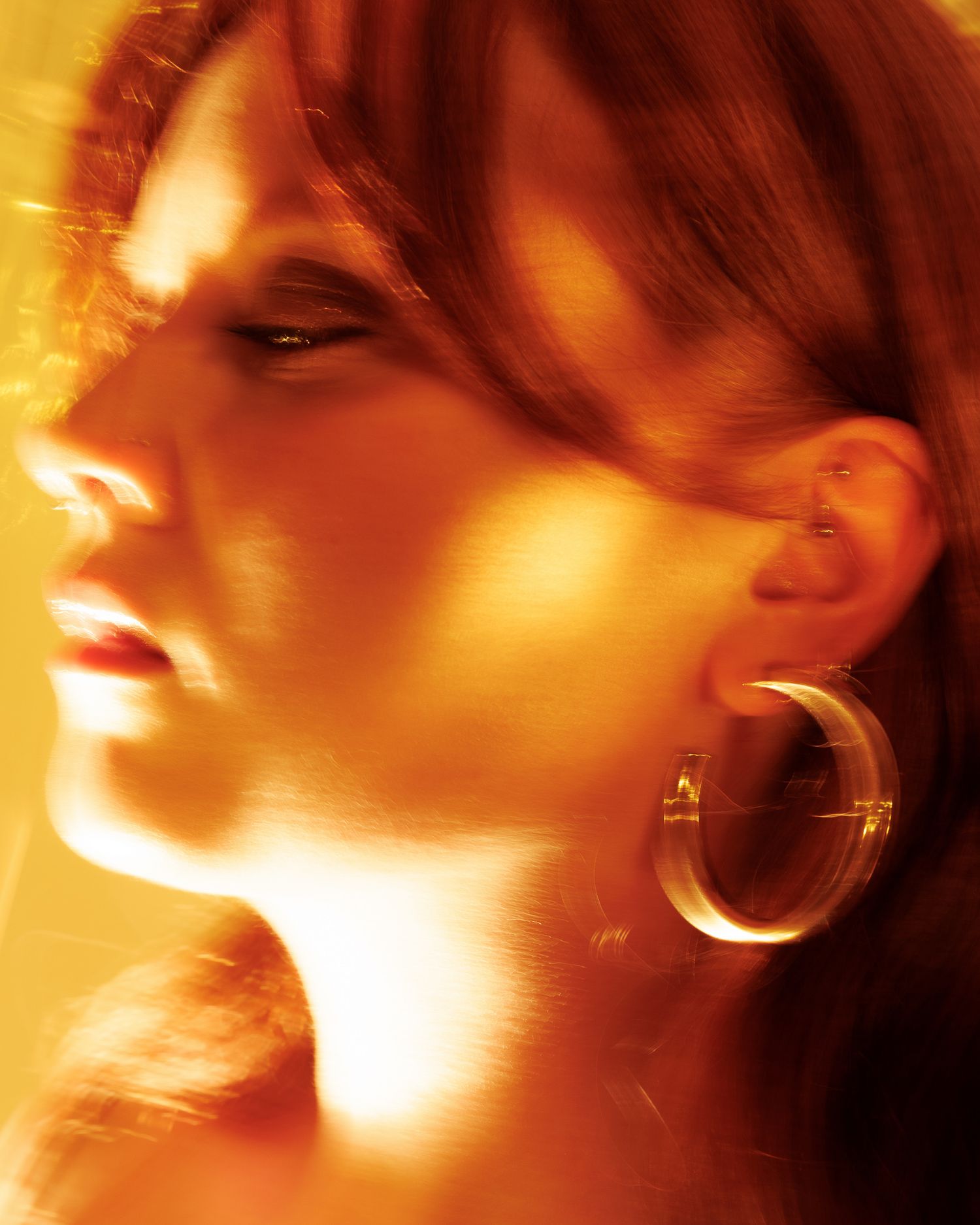 Close-up profile of a woman with hoop earrings bathed in warm golden-orange light.