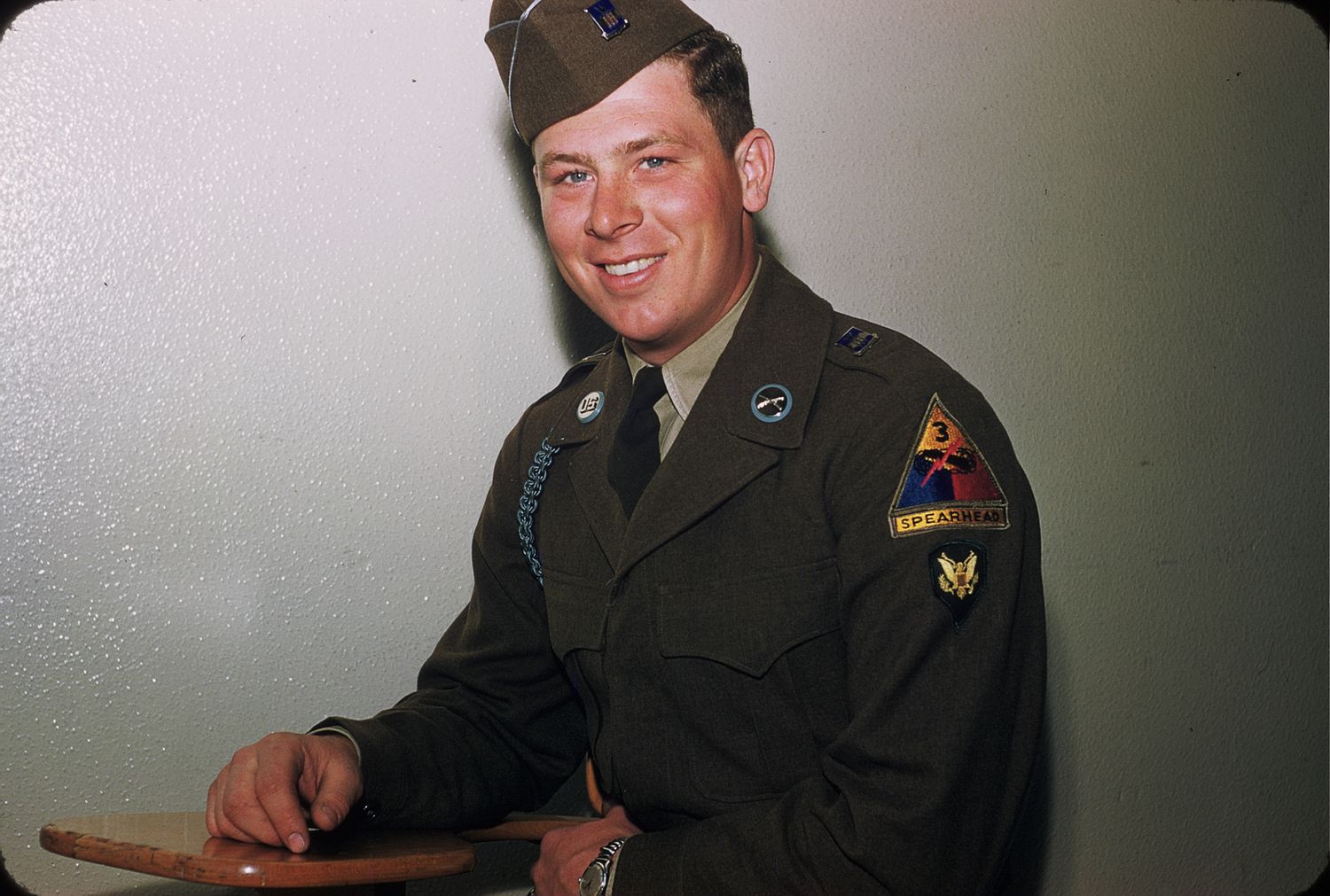 Smiling US Army soldier in dress uniform with patches posing for portrait photo in color.