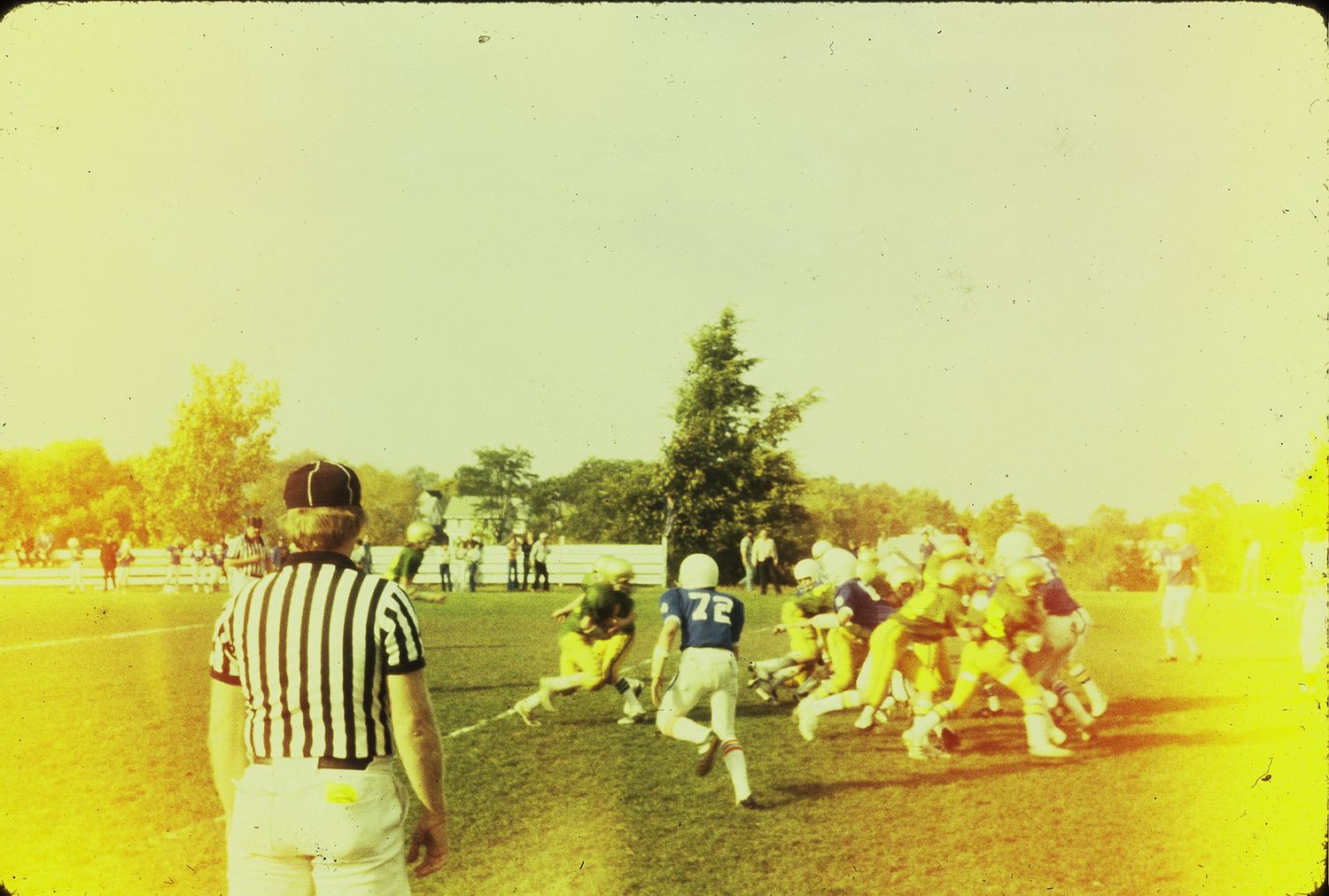 Referee watching football players in a pile during a youth game on a field.