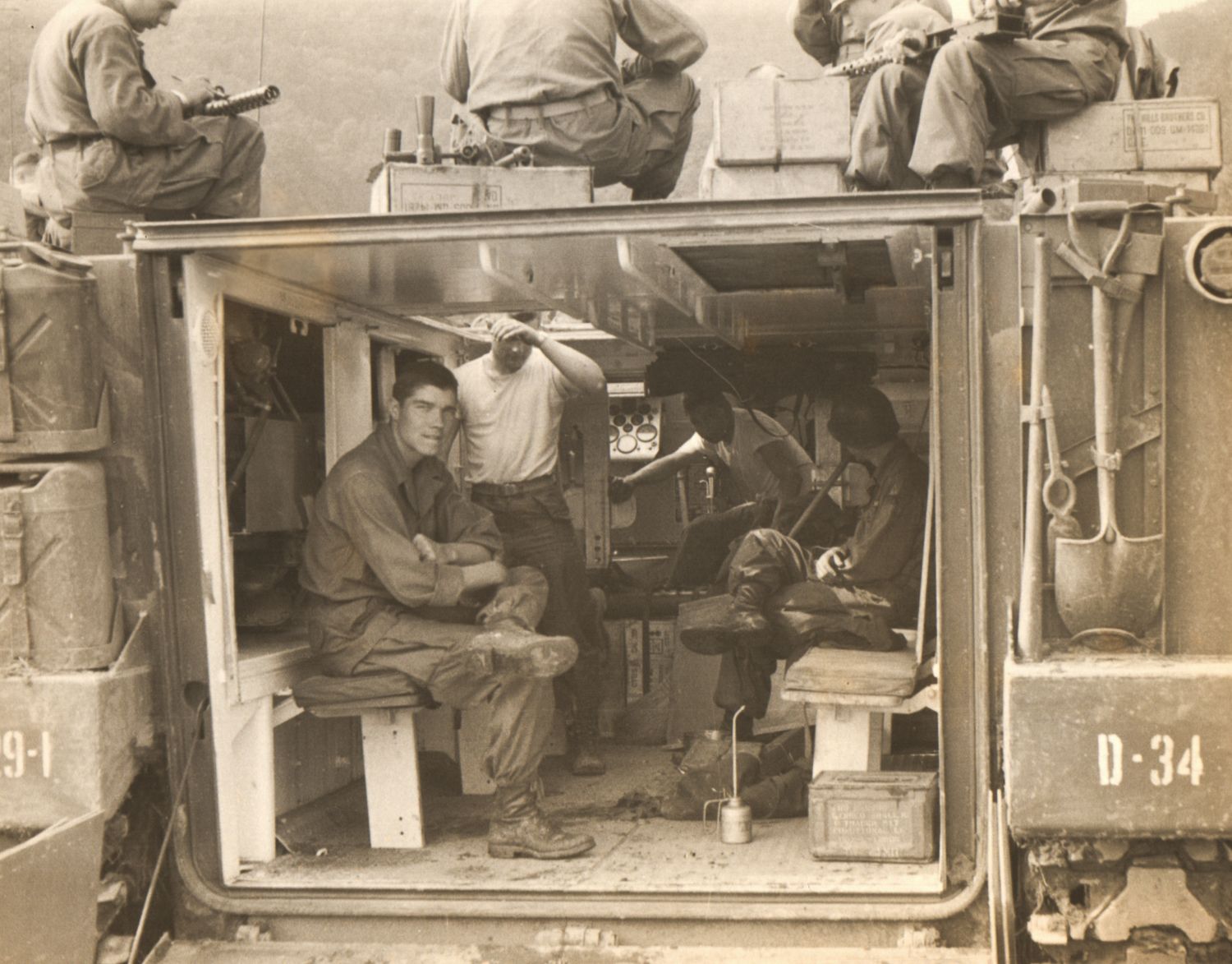 WWII soldiers inside a military vehicle marked D-34, with crew members visible on top in a vintage black and white photo.