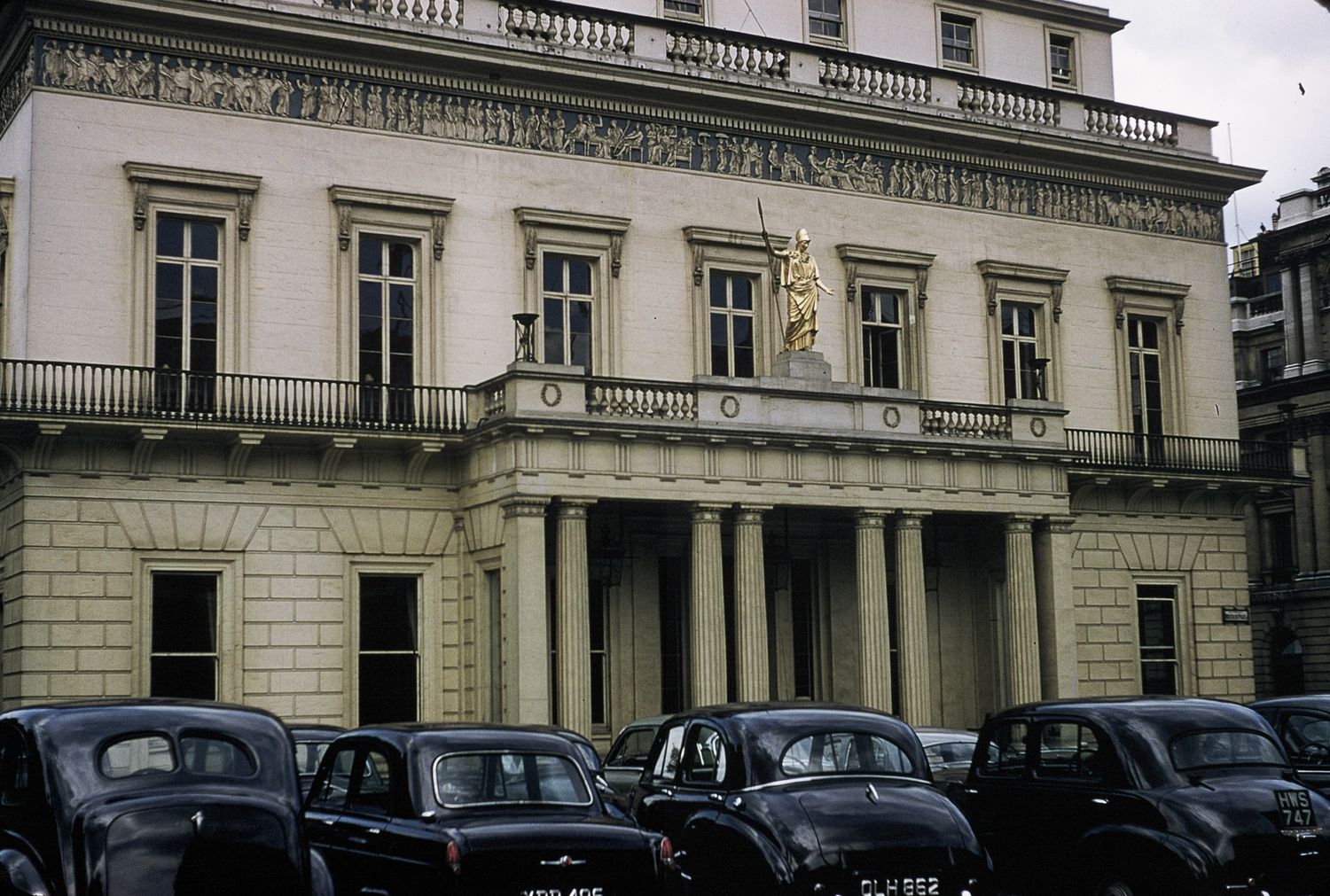 Classic European government building facade with columns and vintage black cars parked outside.