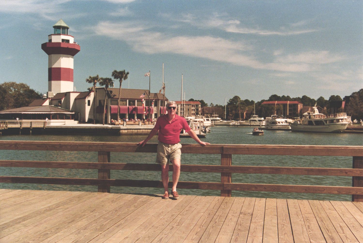 Man posing on wooden pier near red and white striped lighthouse at Harbour Town marina, Hilton Head Island, SC.