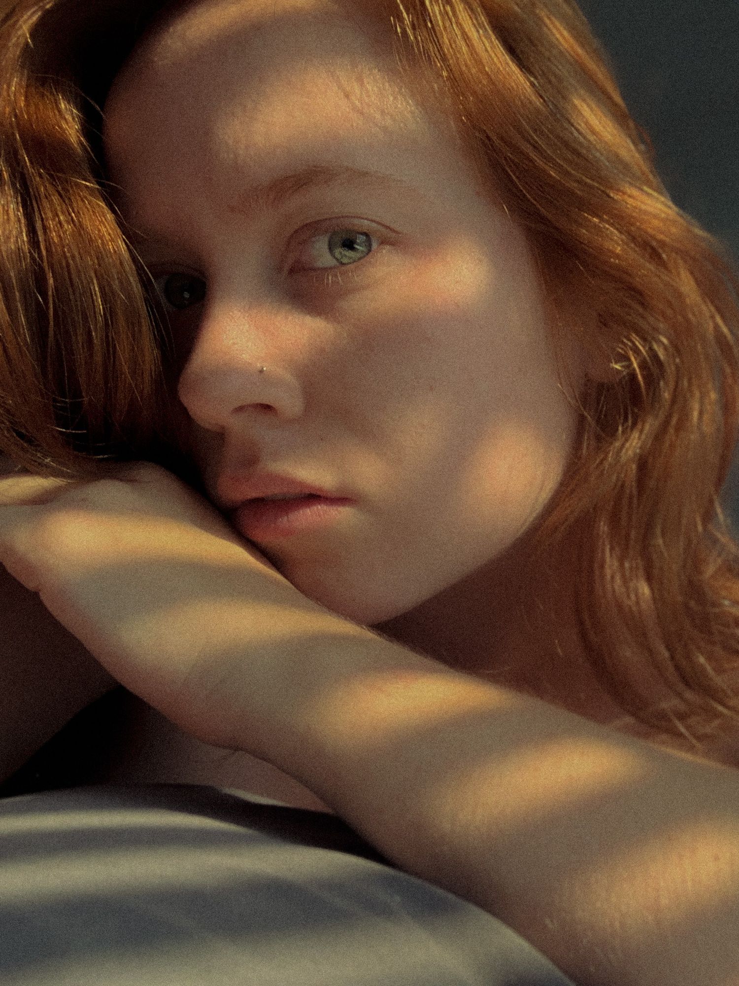 SAINT JAMES PHOTO- Close-up portrait of a redhead woman with freckles resting her head on arms.