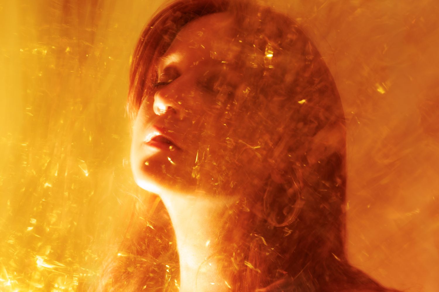 A woman bathed in golden light with shimmering fragments creating a ethereal fiery effect.