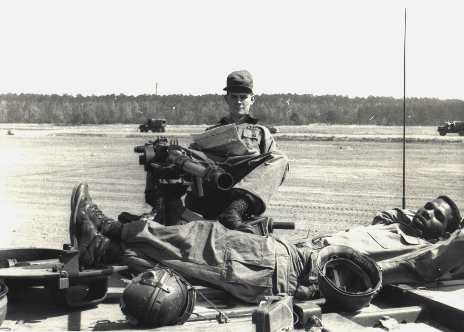 Black and white photo of soldiers resting on military equipment in an open field.