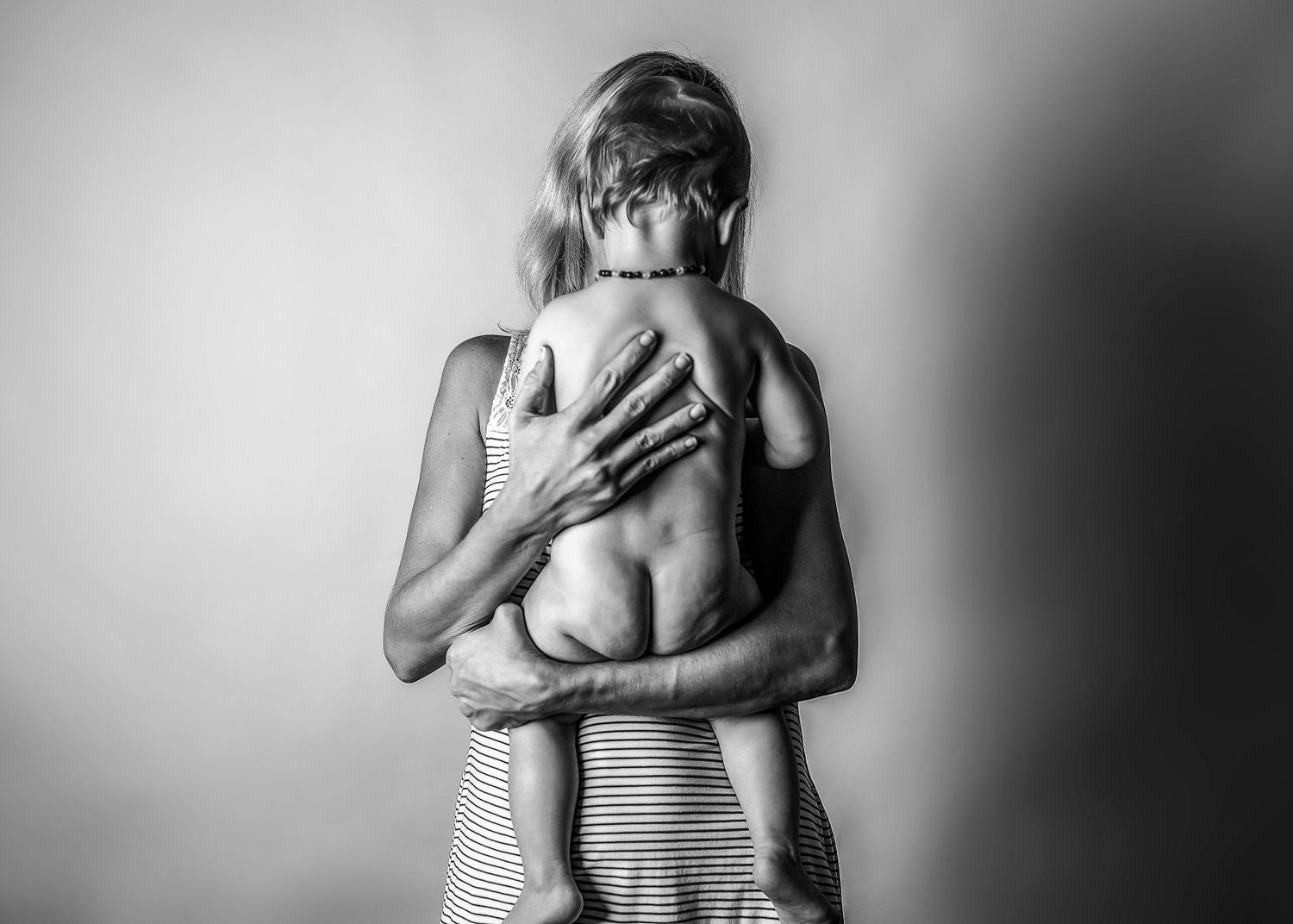 Black and white photo of a woman embracing a child from behind in a tender, intimate moment.