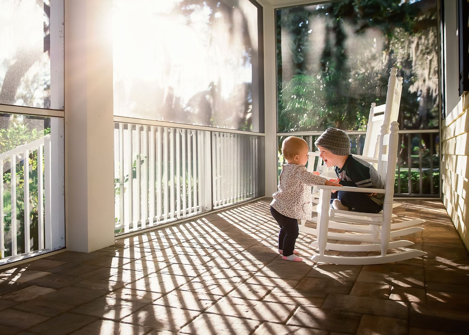 Two young children sharing a tender moment on a sunlit porch with rocking chair.